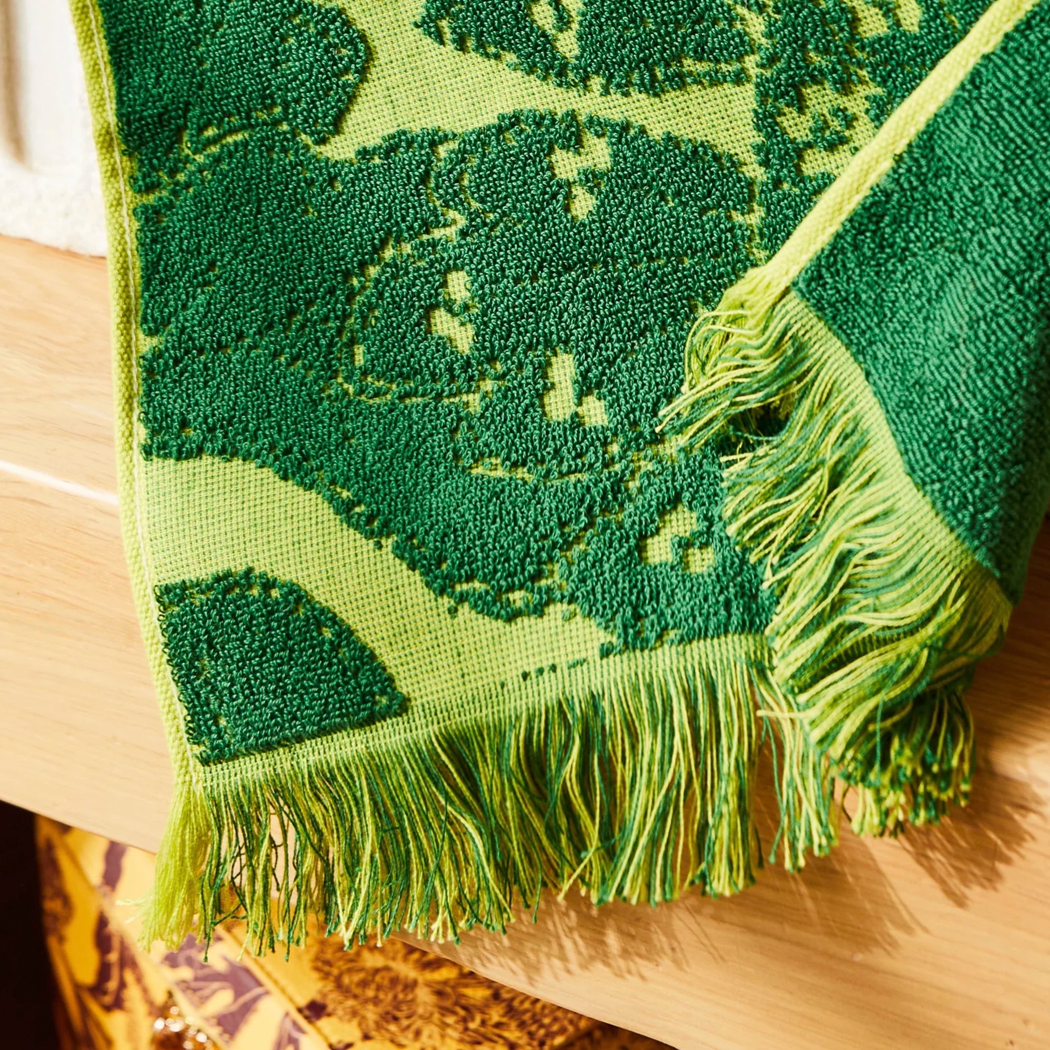 Green textured wash cloth with fringe on a wooden surface