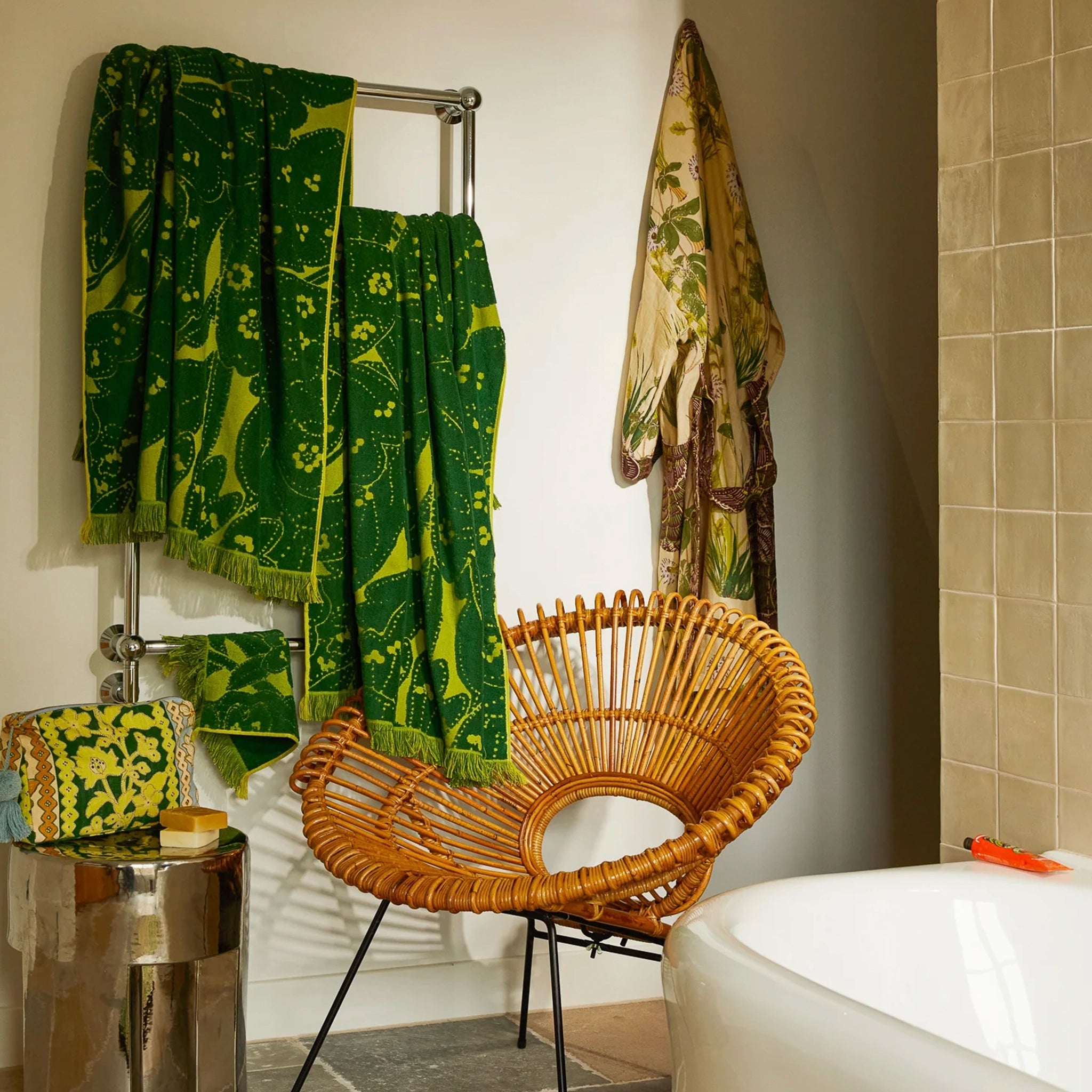 Bathroom with green patterned towels on a rack, wicker chair, and bathtub.