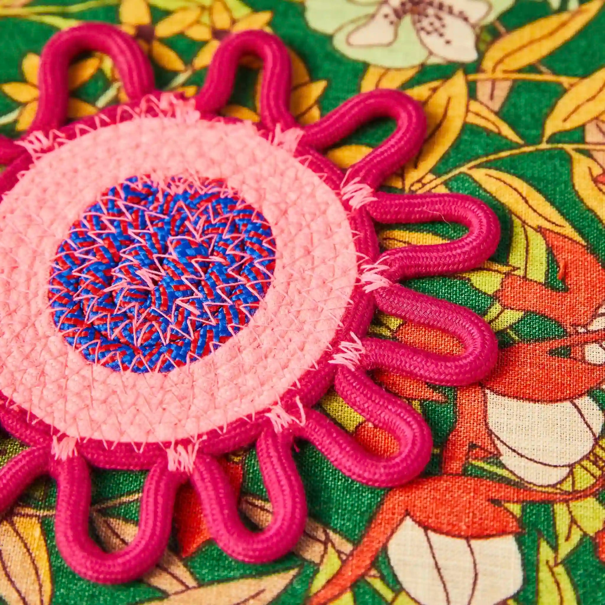 Decorative coaster with pink and blue center on a floral fabric background
