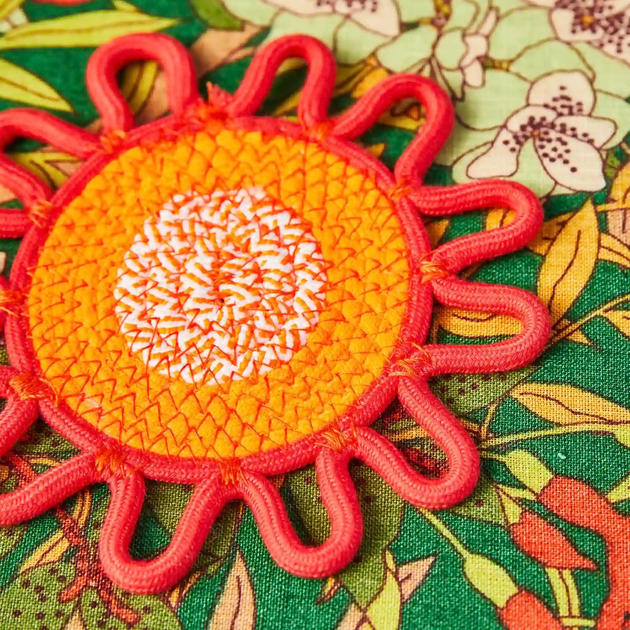 Decorative sun-shaped coaster with orange center and pink rays on a floral fabric background