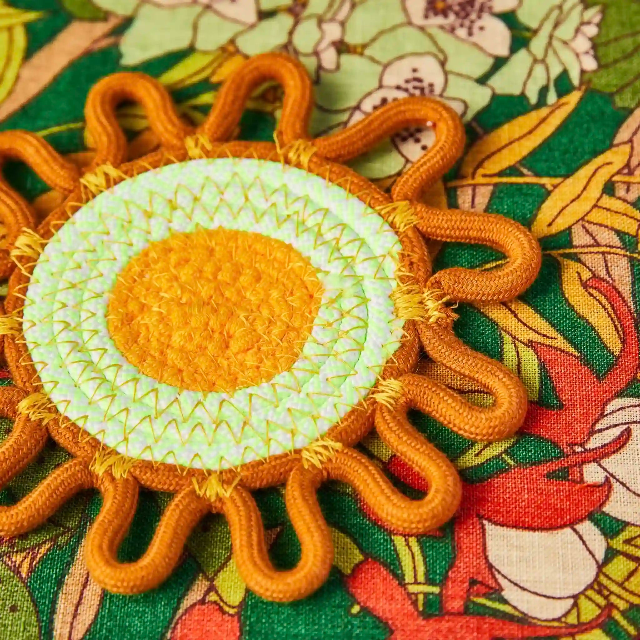 Decorative sun-shaped coaster with orange and green colors on a floral fabric background