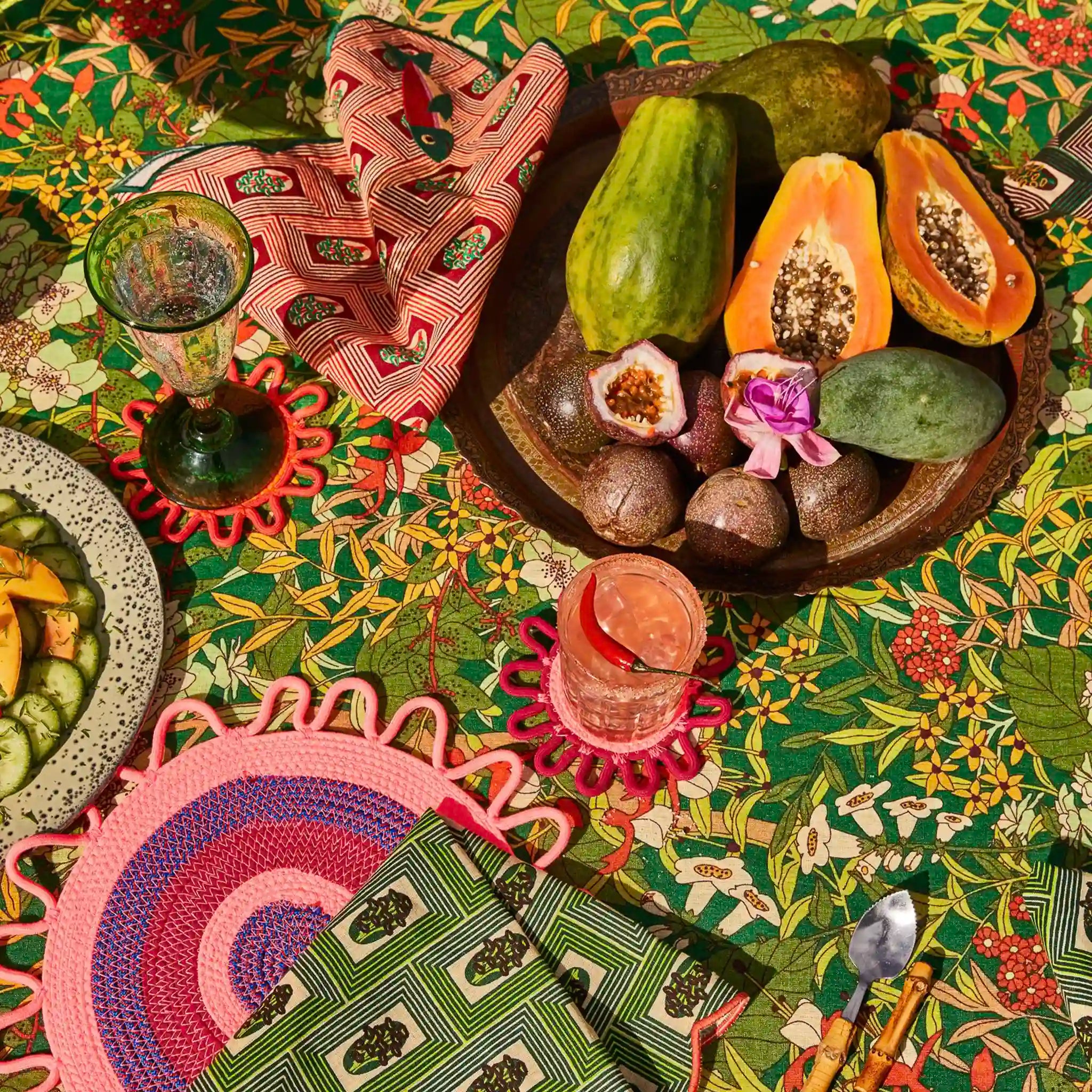 Colorful table setting with fruits, glasses, and decorative items on a patterned tablecloth.