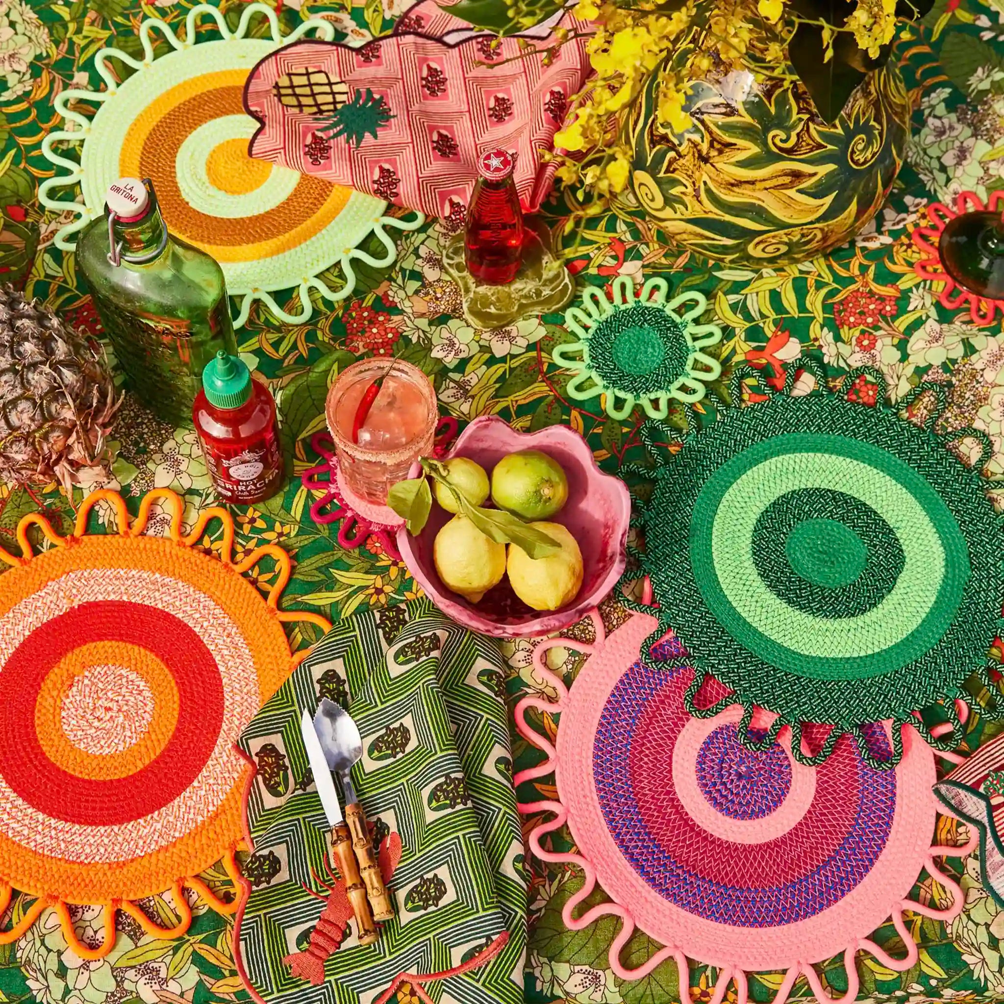 Colorful table setting with patterned placemats and cutlery on a floral tablecloth.
