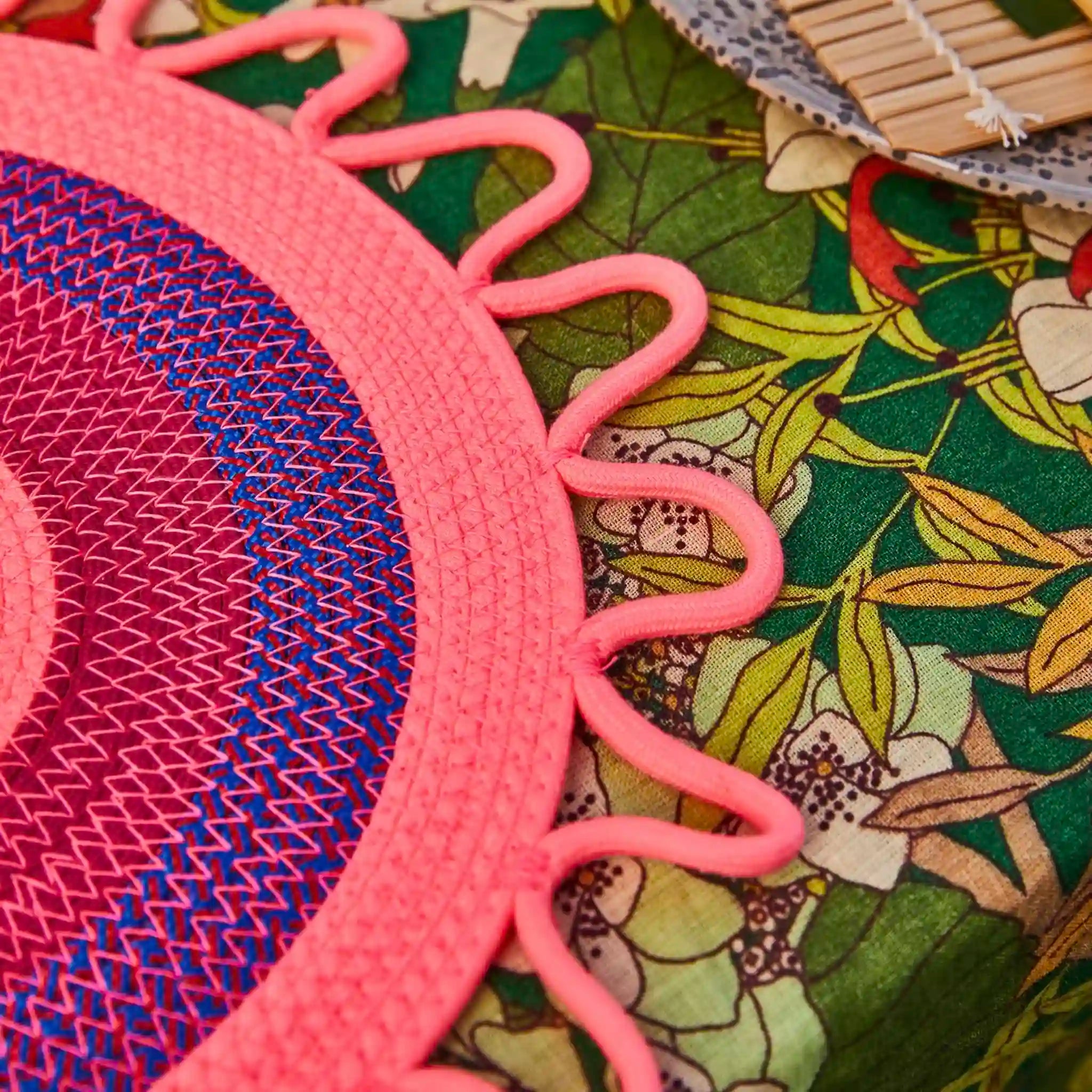 Close-up of a pink woven placemat with a floral-patterned fabric background