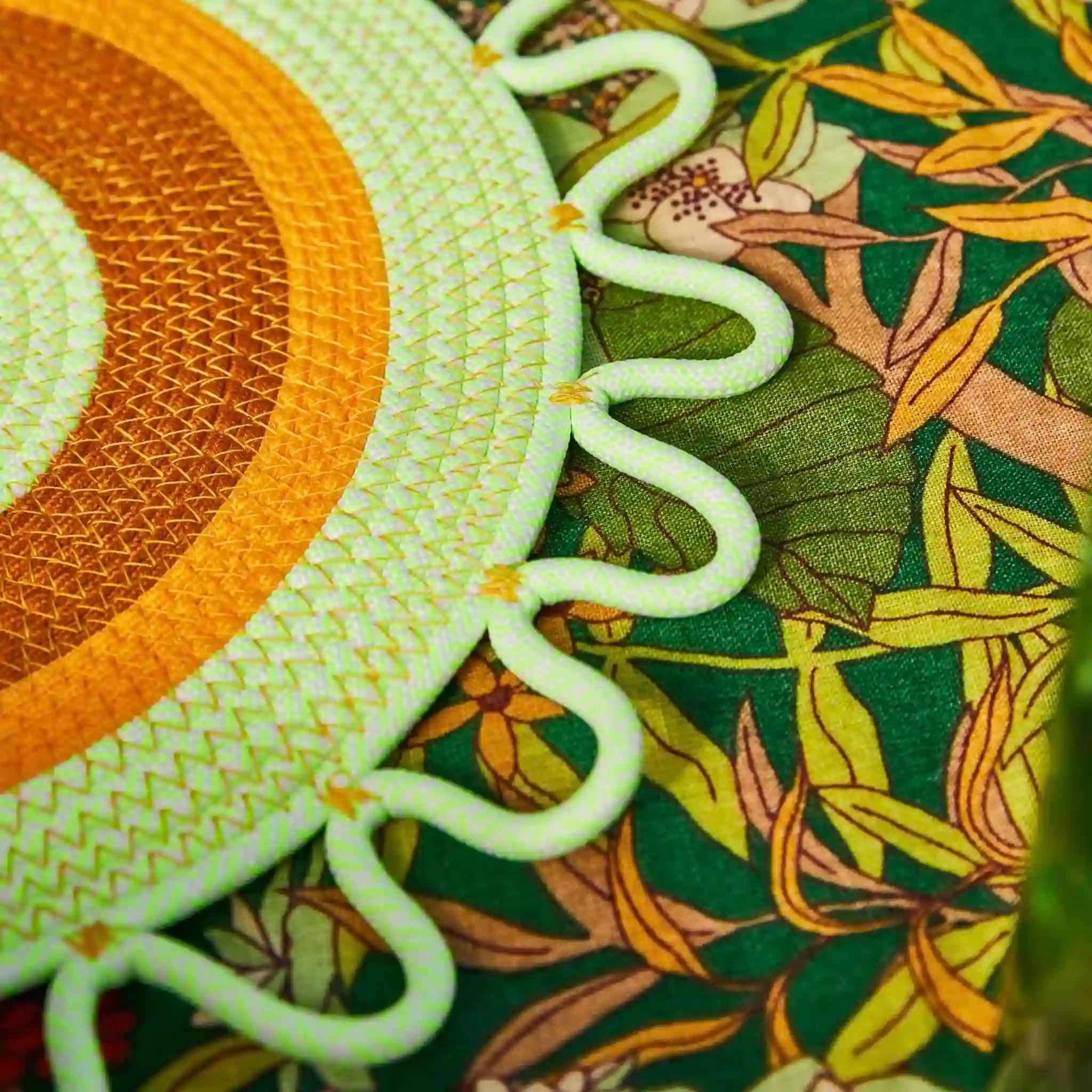 Close-up of a textured green and orange placemat on a leaf-patterned fabric background