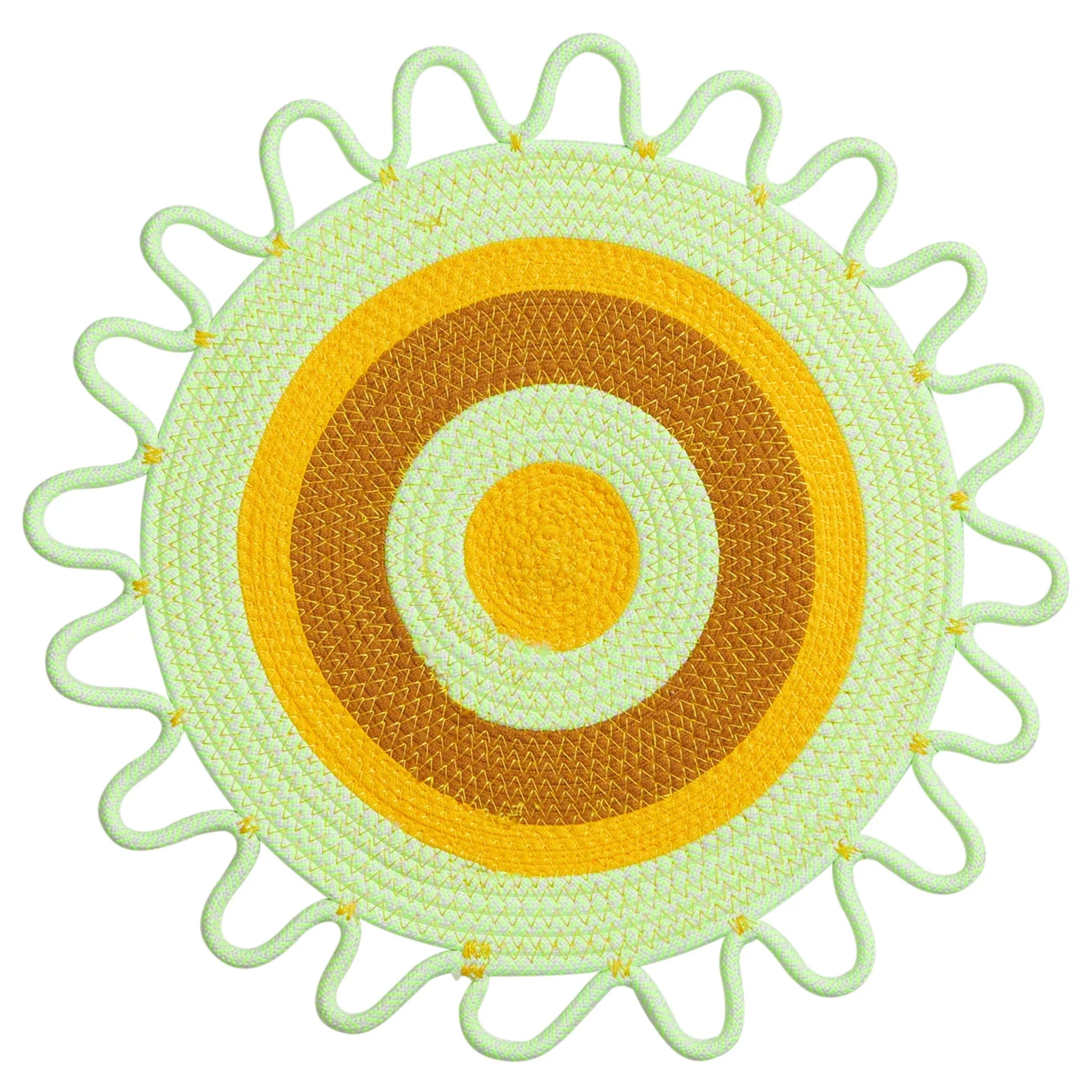Round woven placemat with concentric circles in green, yellow, and brown on a white background