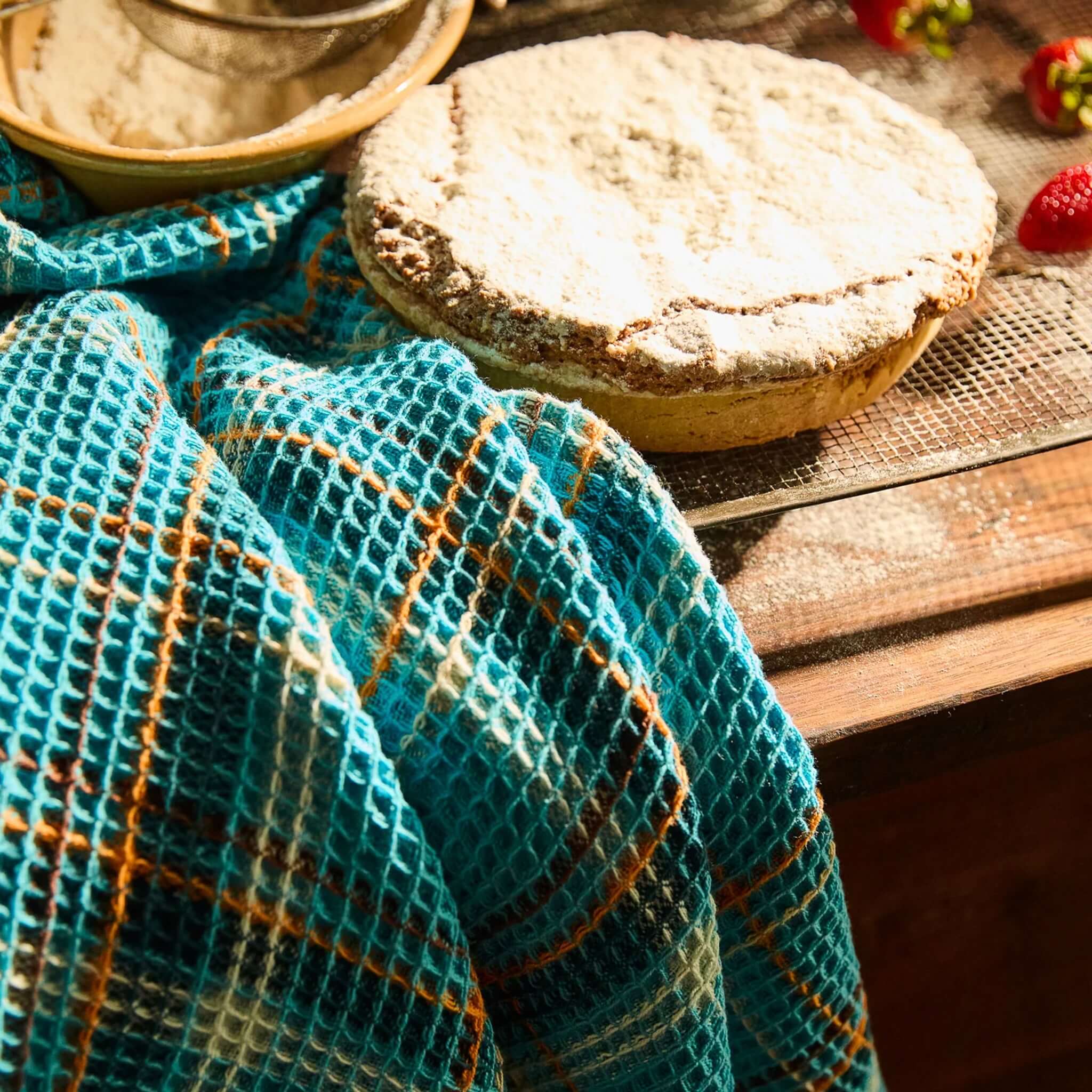 Sage x Clare Frances Organic Cotton Waffle Tea Towel - Turquoise draped over a wooden table with a baked cake.