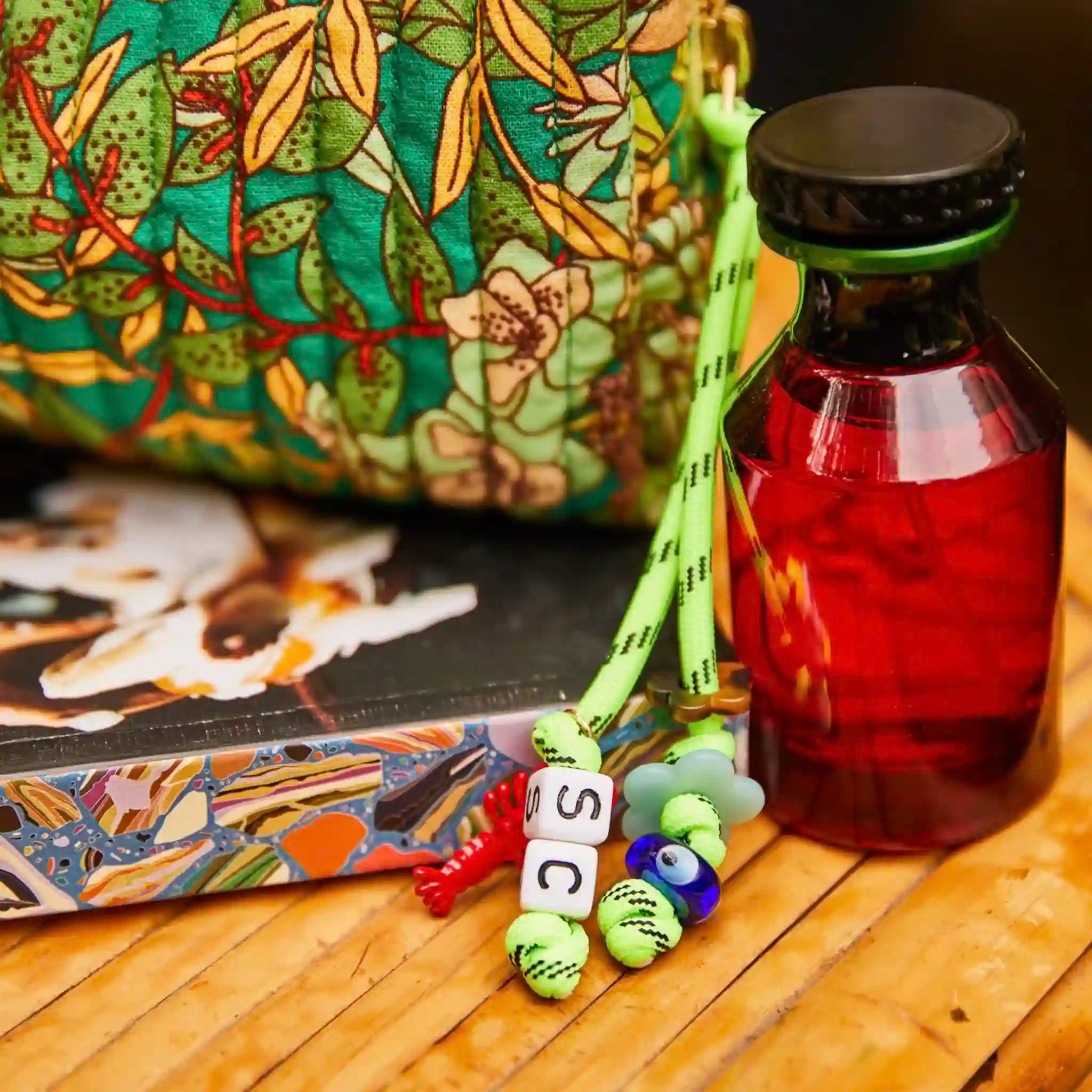 Colorful lanyard with charms on a wooden surface next to a bottle and patterned bag.