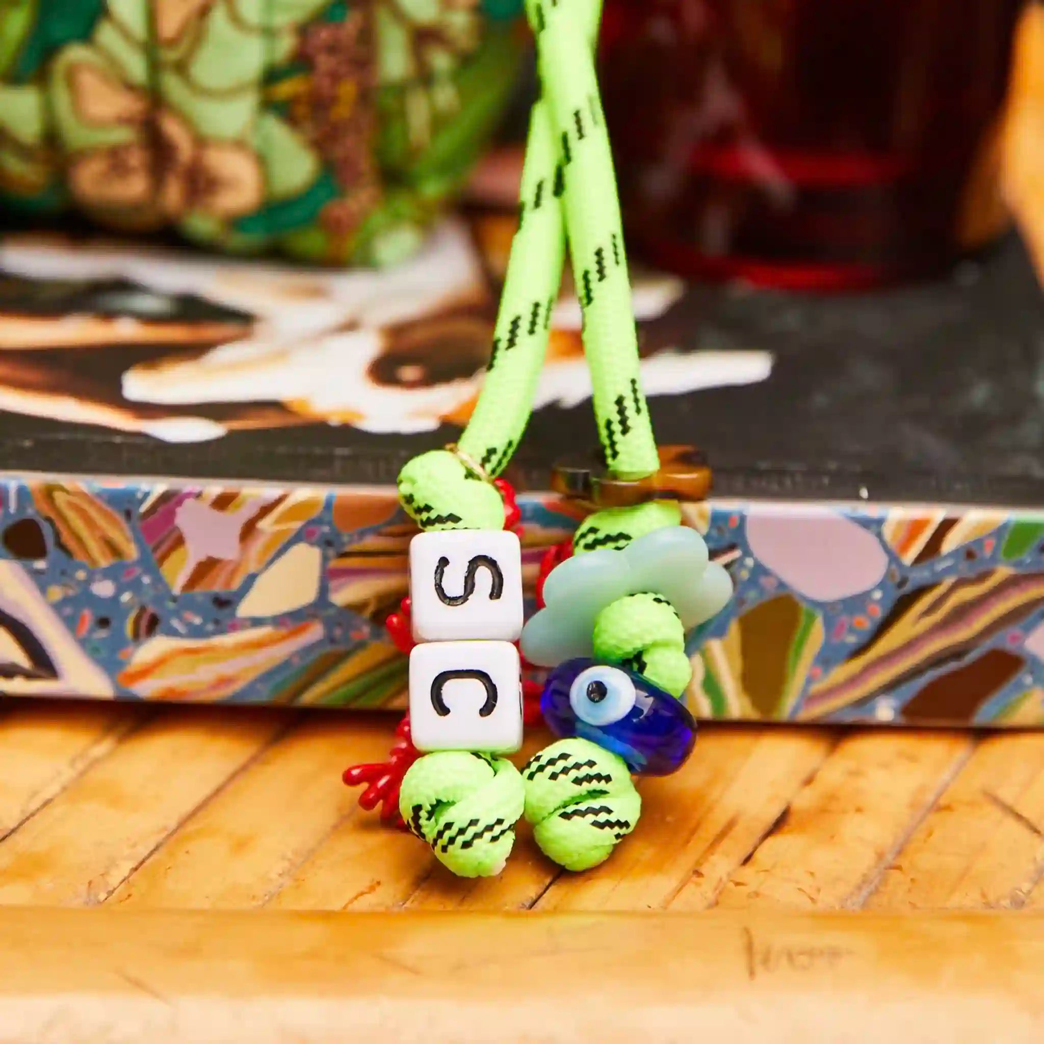 Colorful phone charm with beads spelling 'SC' on a wooden surface
