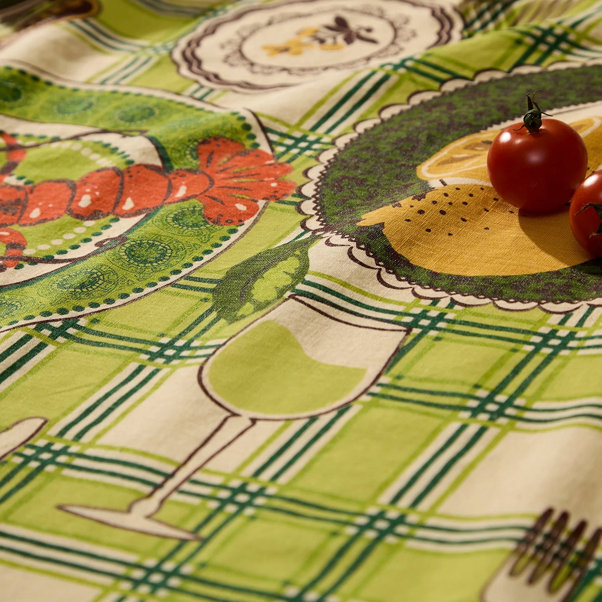 Close-up of a colorful tablecloth with food illustrations and tomatoes on a patterned background.