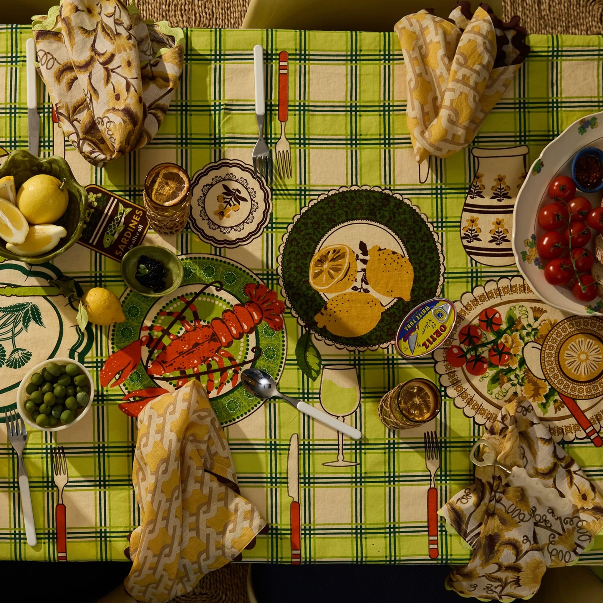 Decorative table setting with various plates, cutlery, and food items on a green checkered tablecloth.