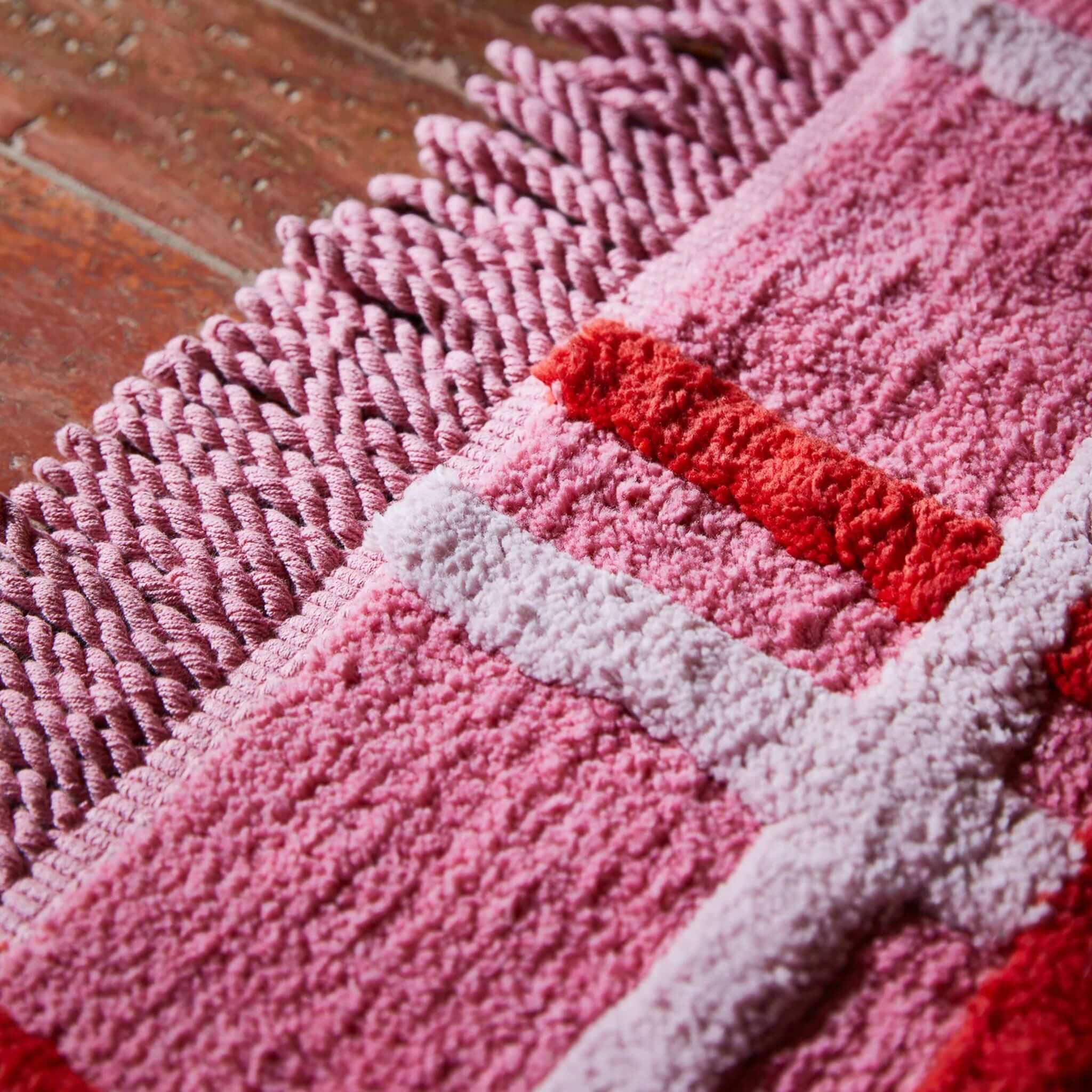 Sage x Clare Karina Bath Mat - Rosewood, showcasing vibrant colors and plush texture with decorative fringe trim.