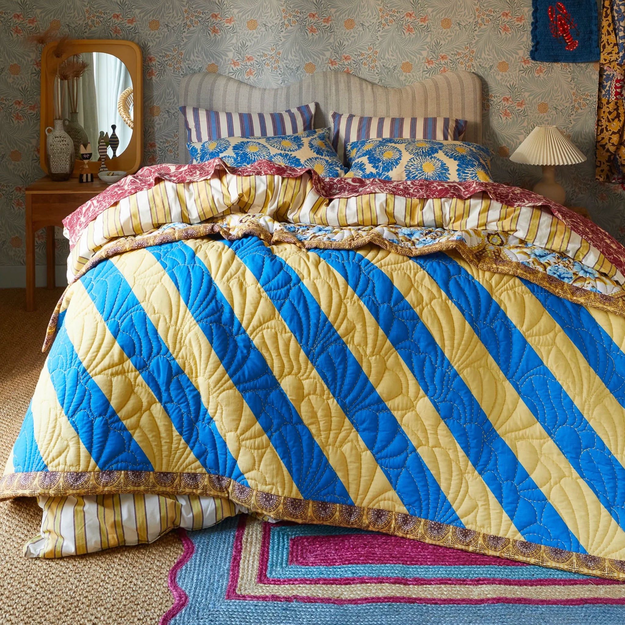 Bed with a colorful striped quilt in a room with patterned wallpaper.