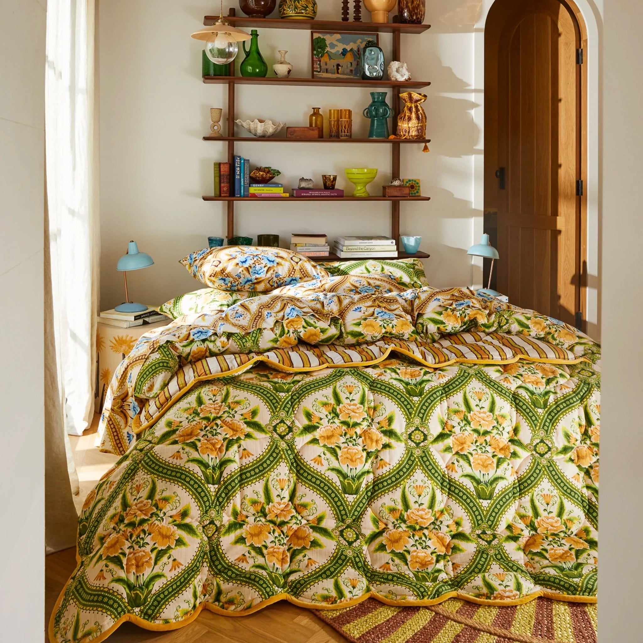 Decorative quilt with floral pattern on a bed in a room with shelves and books.