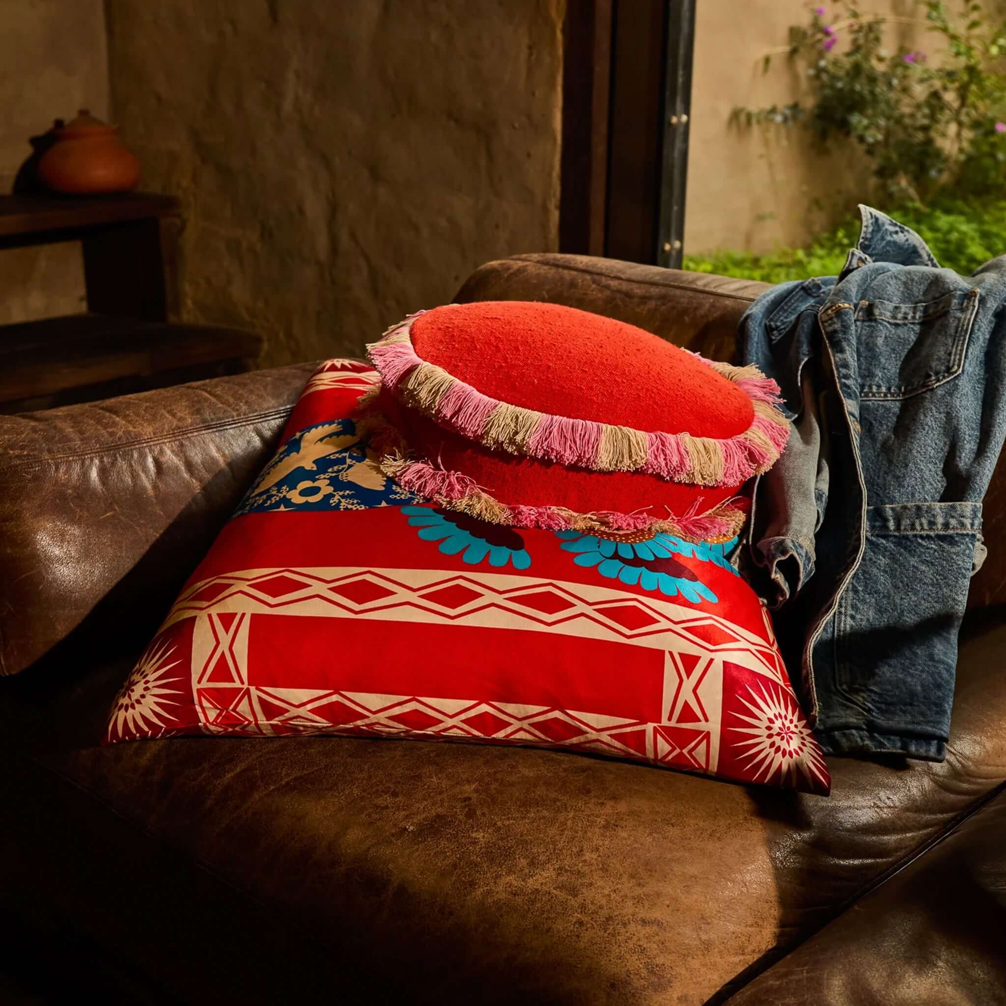 Sage x Clare Reese Round Cushion - Poppy on a leather couch with two-tone fringe design and floral patterns.