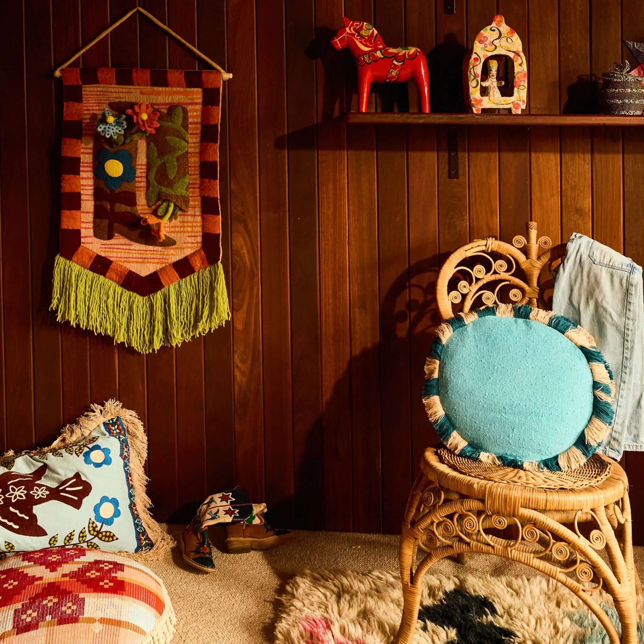 Sage x Clare Reese Round Cushion - Turqouise on a rattan chair amidst colorful decor.