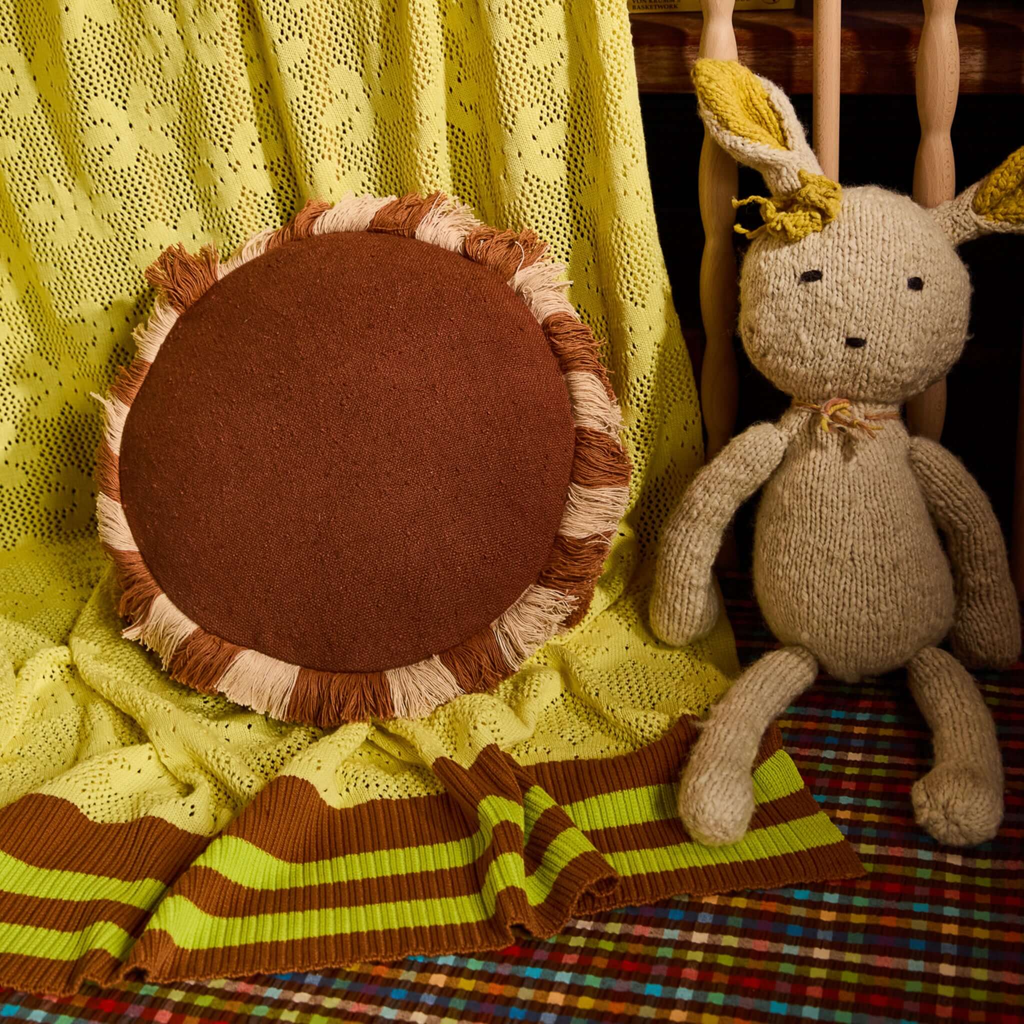 Sage x Clare Reese Round Cushion - Umber on a vibrant yellow blanket with a knitted toy beside it.