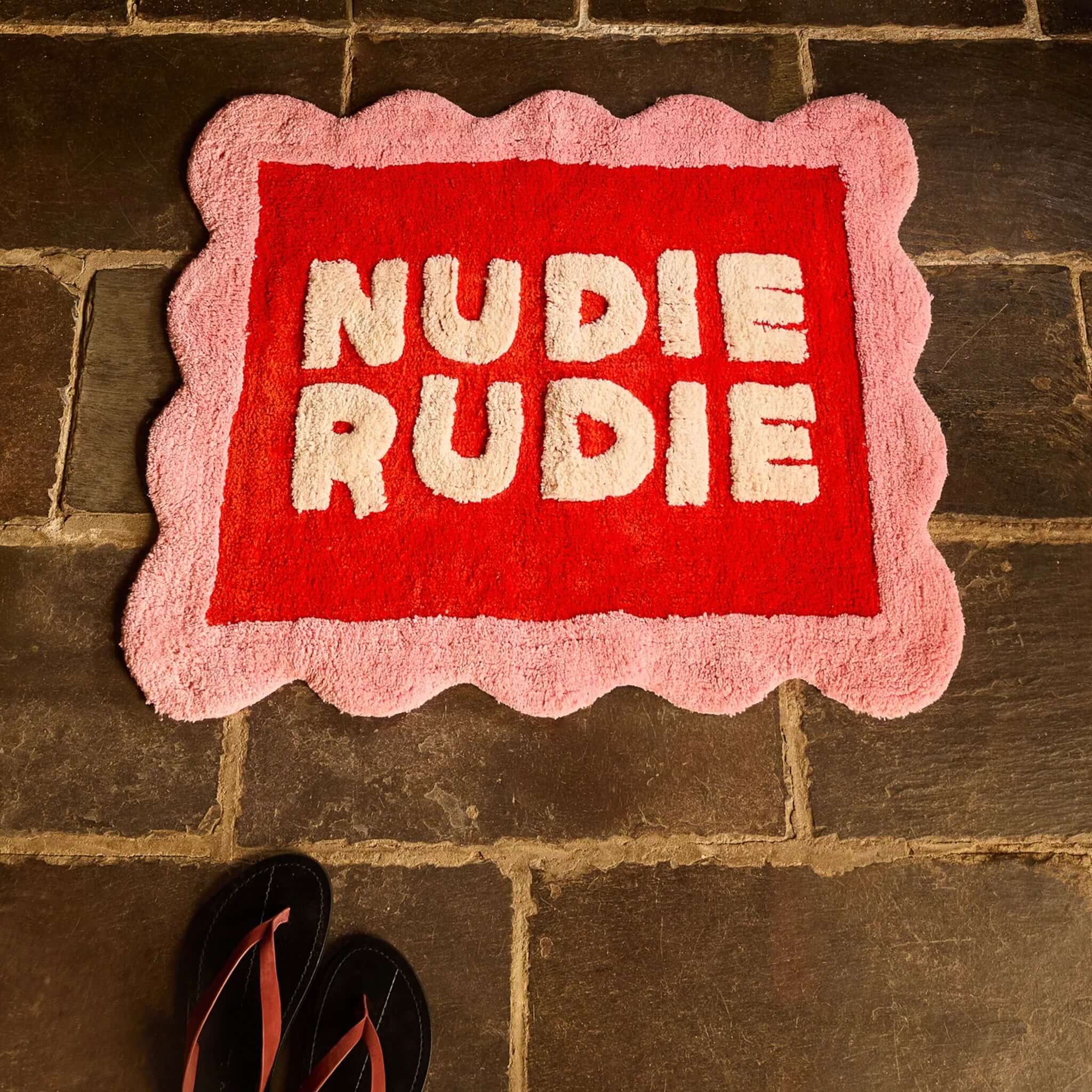 Sage x Clare Romy Nudie Bath Mat - Poppy with plush cream lettering on red, framed by a pink scalloped border.