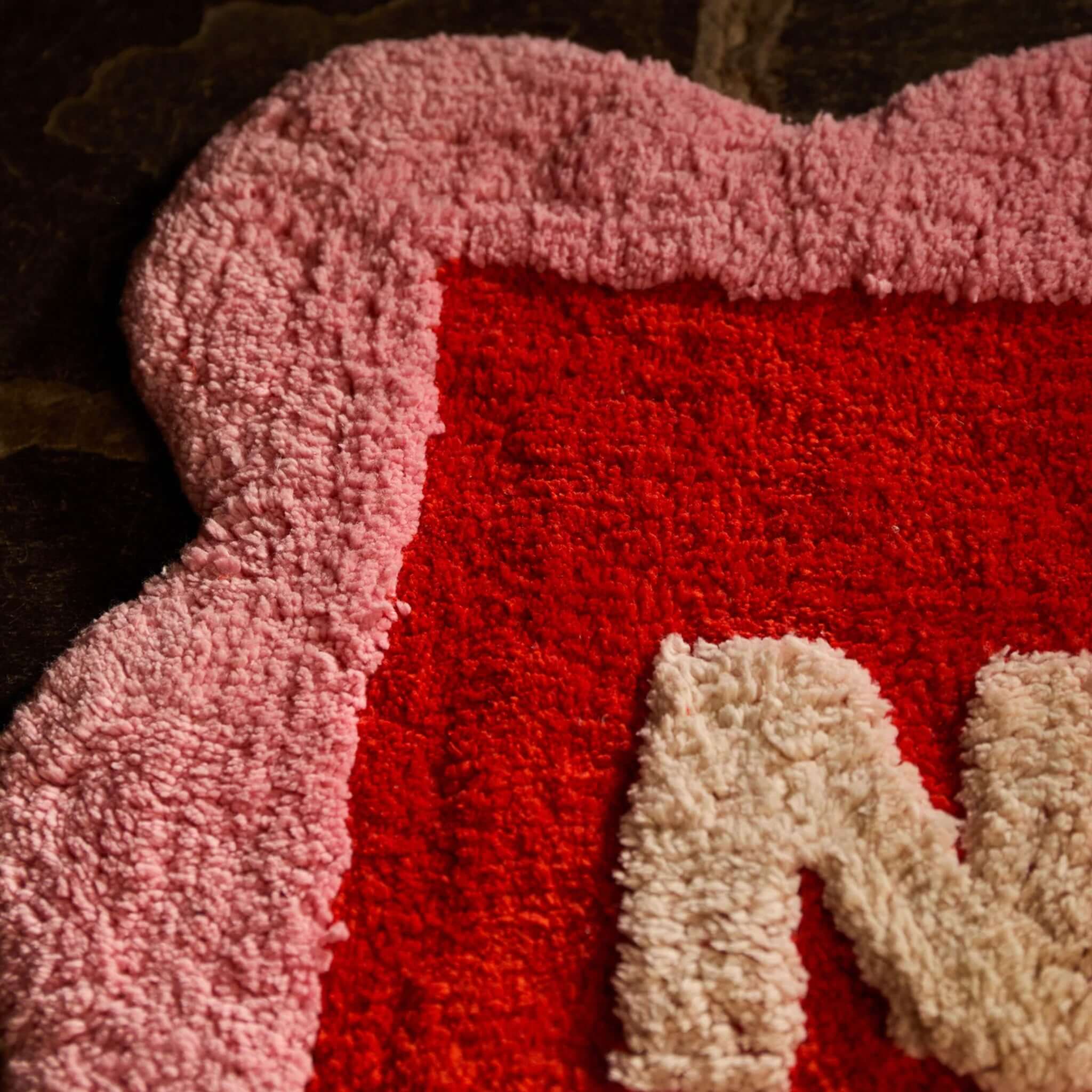 Sage x Clare Romy Nudie Bath Mat - Poppy with scalloped pink border and cream lettering on bold red background.