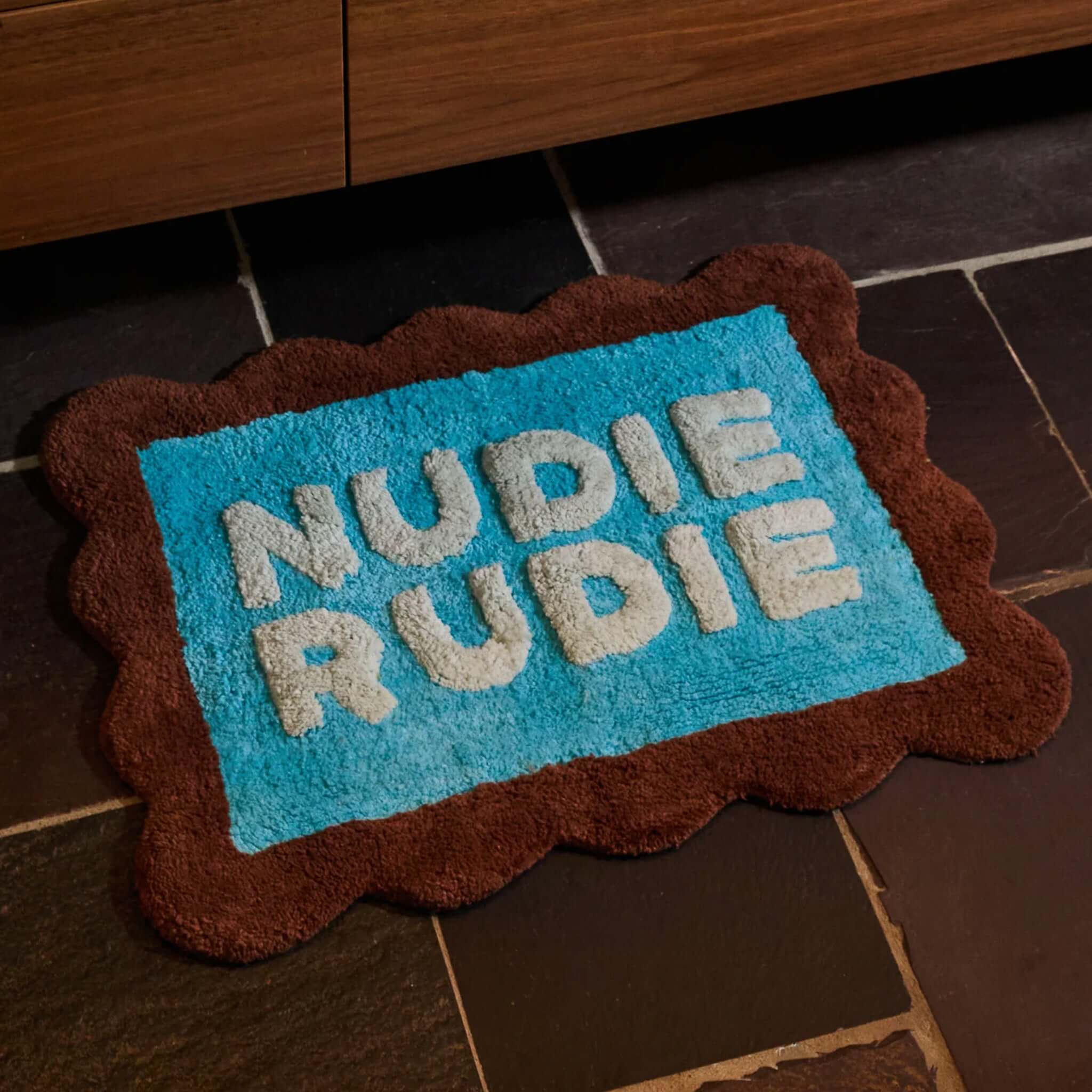 Sage x Clare Romy Nudie Bath Mat Mini - Turquoise with "Nudie Rudie" lettering on a playful turquoise backdrop.