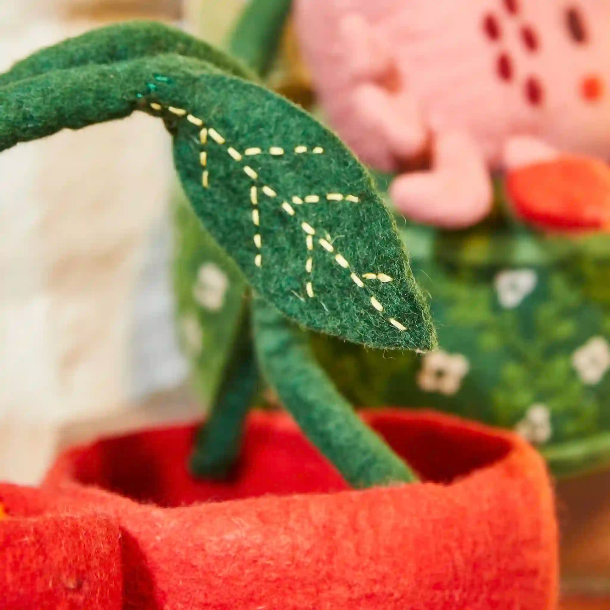 Close-up of a felt plant with green leaves and red pot, with a blurred background.