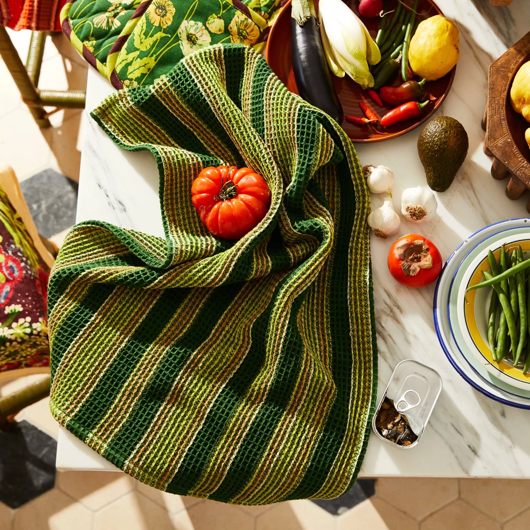 Green and yellow striped tea towel on a table with various vegetables and a phone.