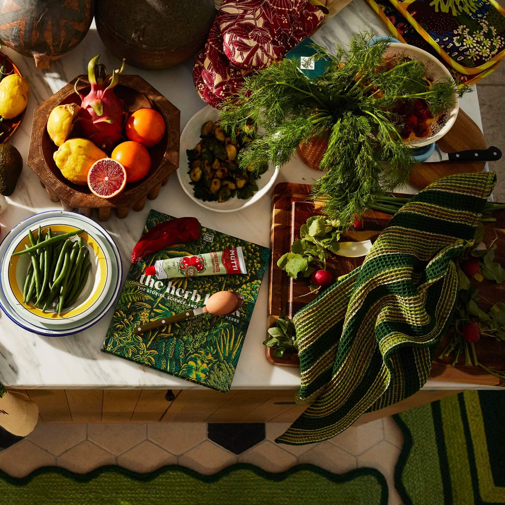 Tabletop scene with fresh produce, a book titled 'The Herb' on a green tea towel.