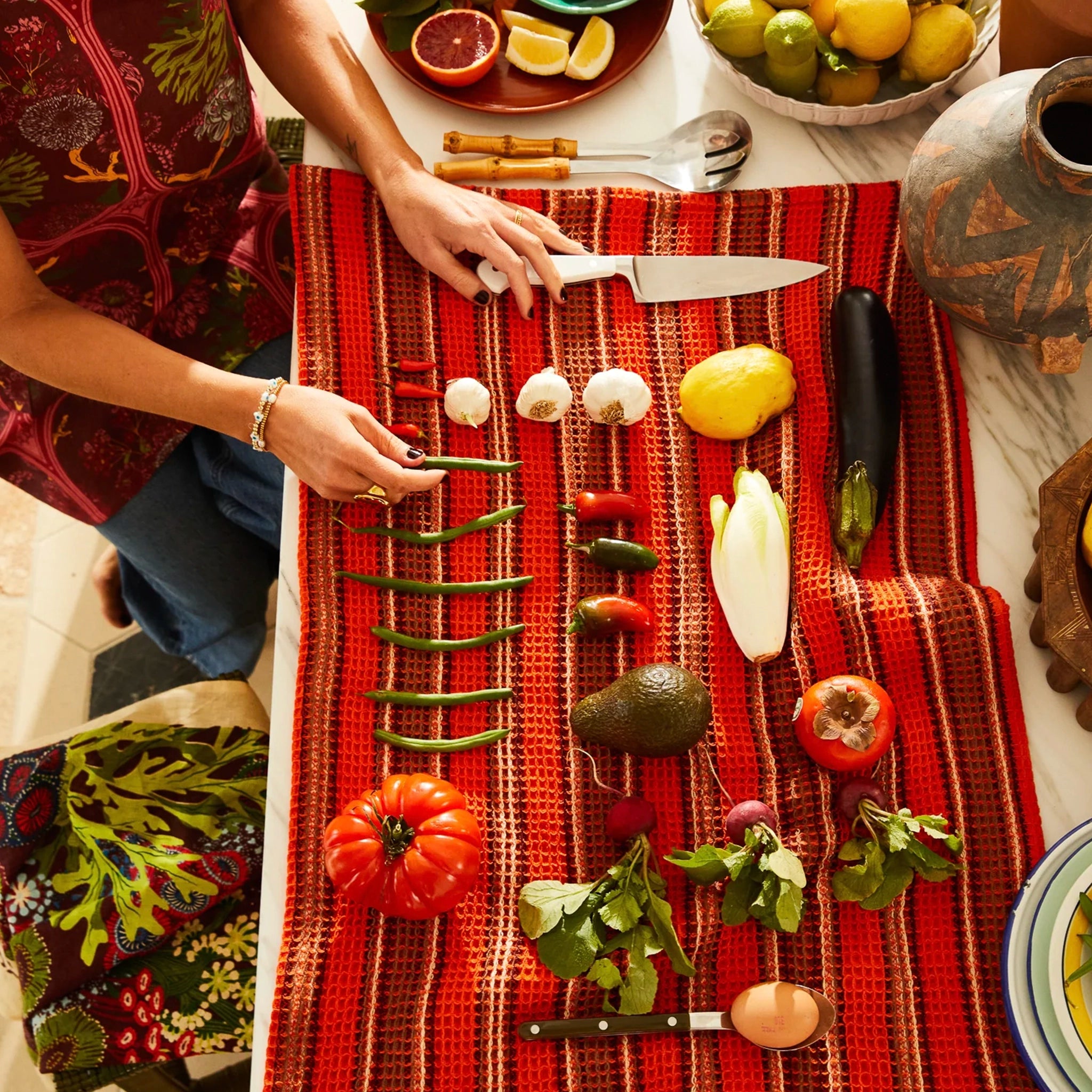 Person preparing vegetables on a red checkered tea towel with various kitchen items.