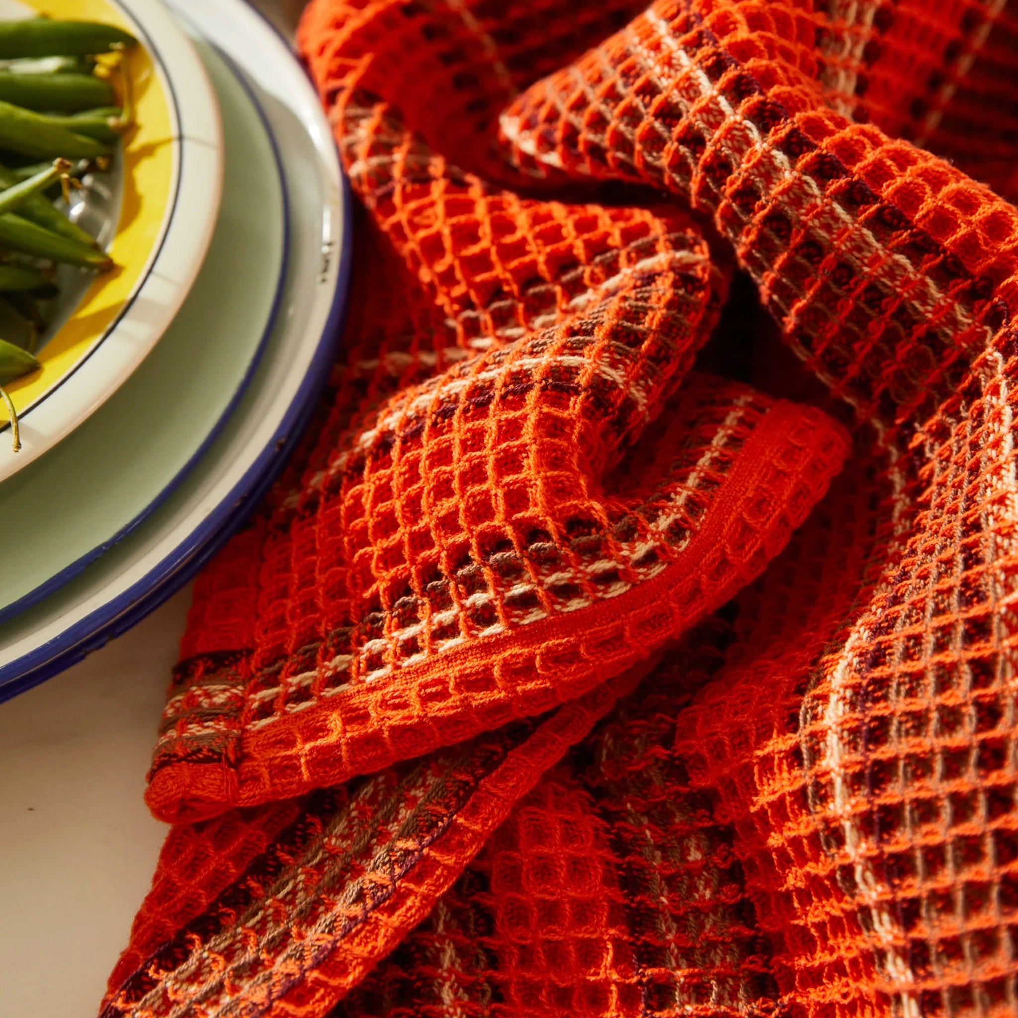 Close-up of a red woven tea towel with green beans on a plate in the background
