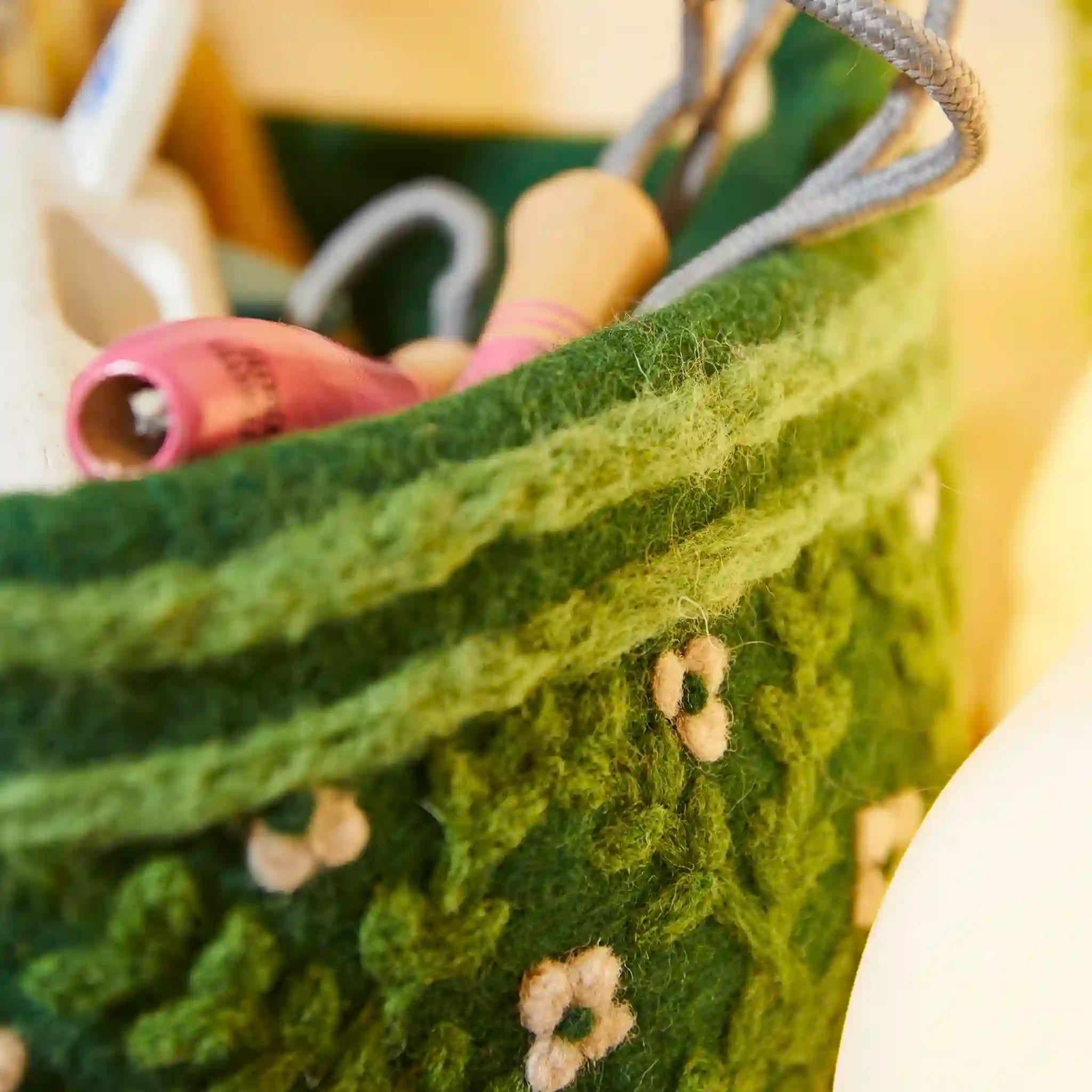 Close-up of a green knitted basket with floral patterns and pink spools of thread.
