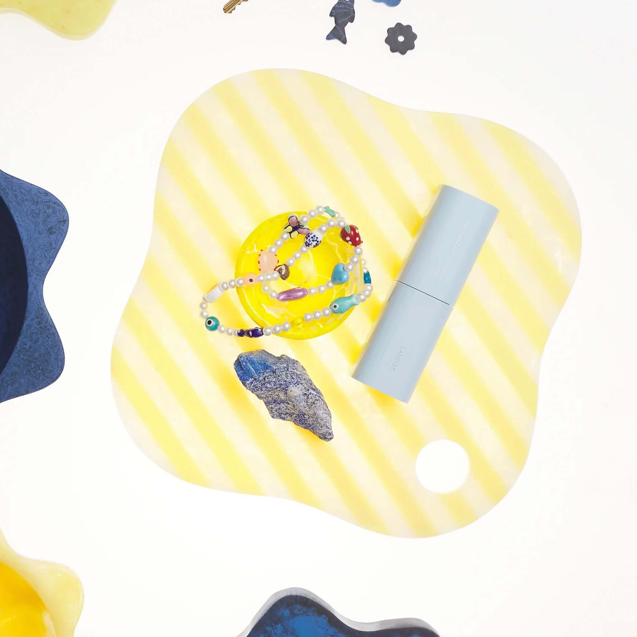 Sage x Clare Theresa Resin Board - Aspen Gold with colorful accessories and jewelry on a striped surface.