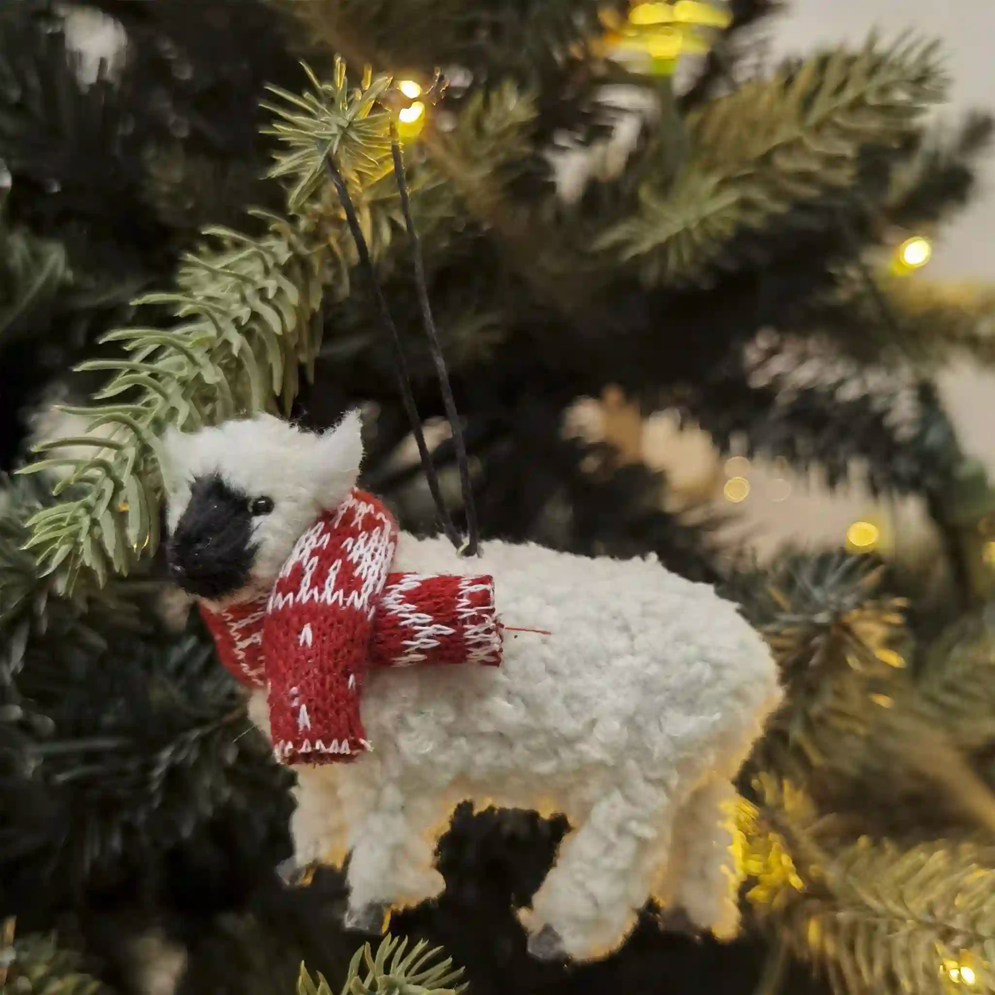 Polar bear ornament wearing a red sweater on a Christmas tree.