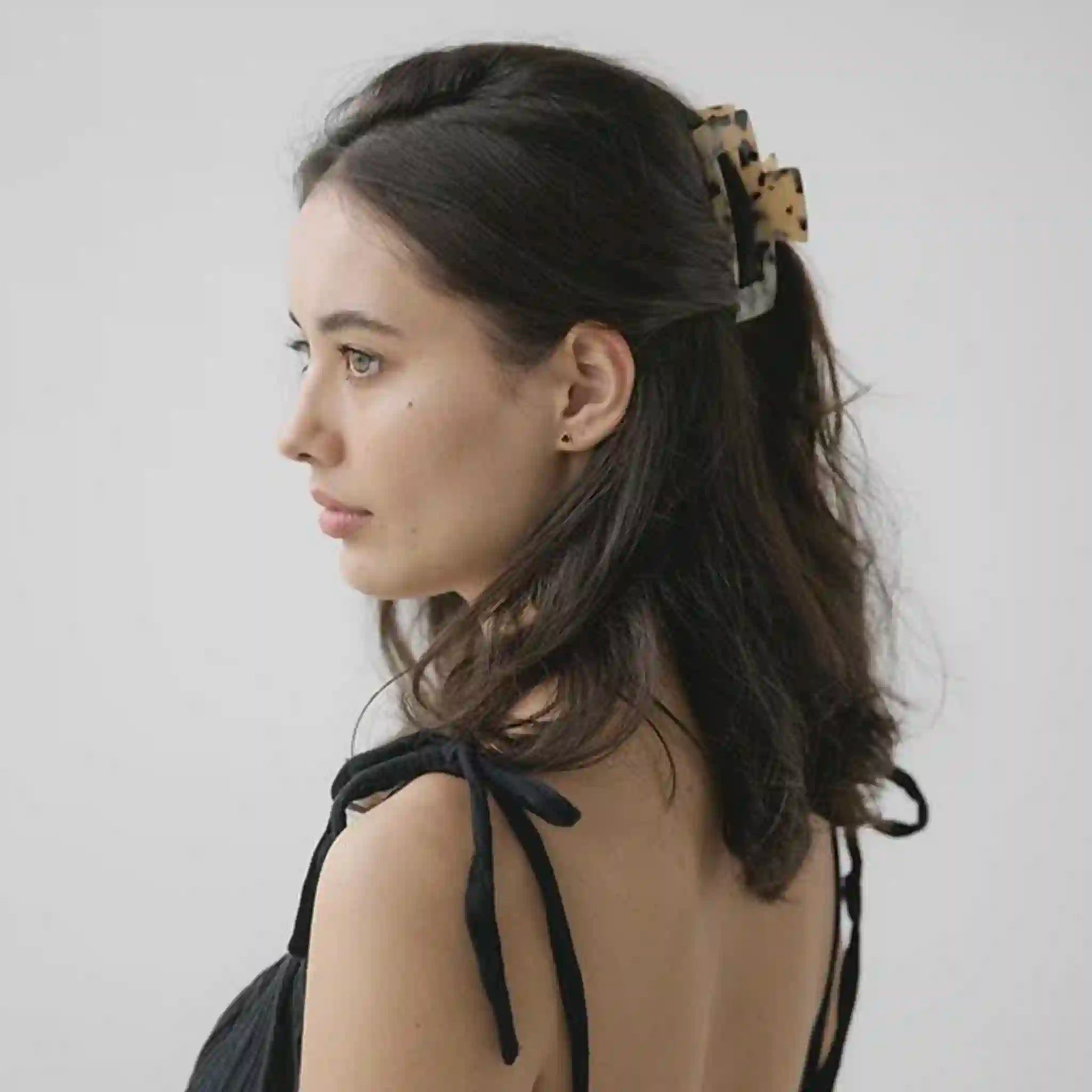 Woman with ponytail wearing a leopard print scrunchie on a plain background