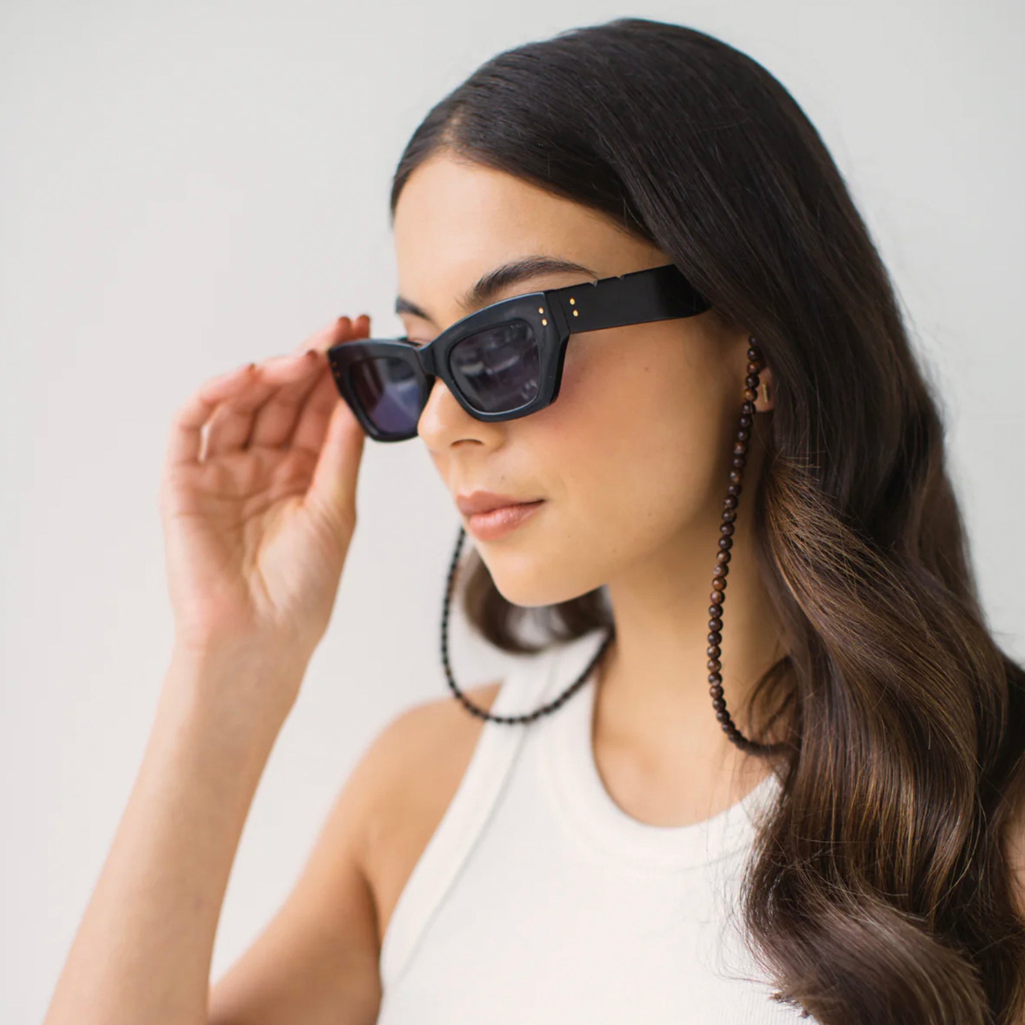 Woman wearing black sunglasses with a chain, against a plain background
