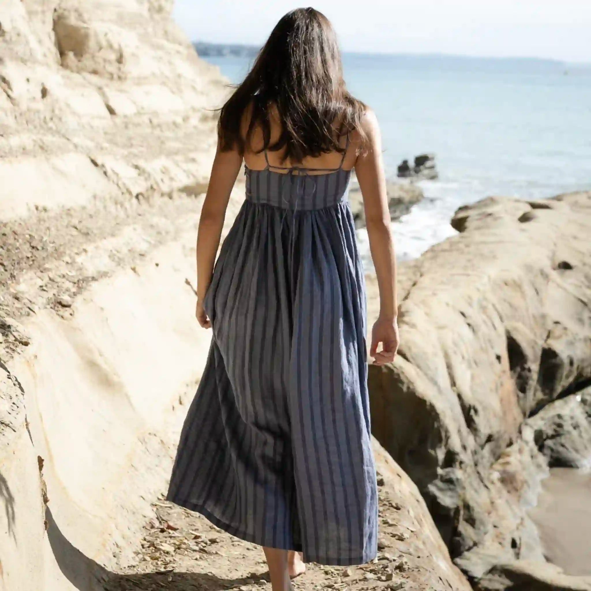 Woman in a blue striped dress standing on a rocky beach.