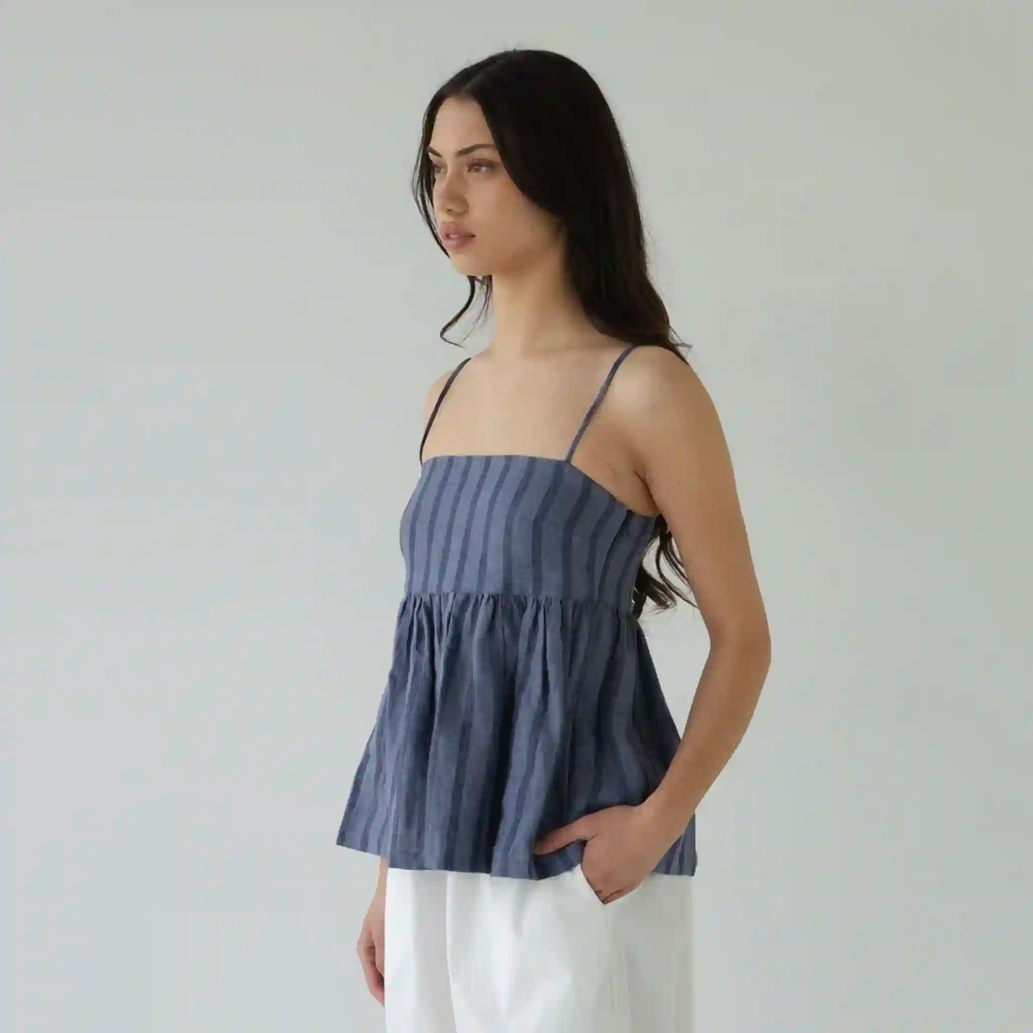 Woman wearing a blue striped top and white pants against a plain background