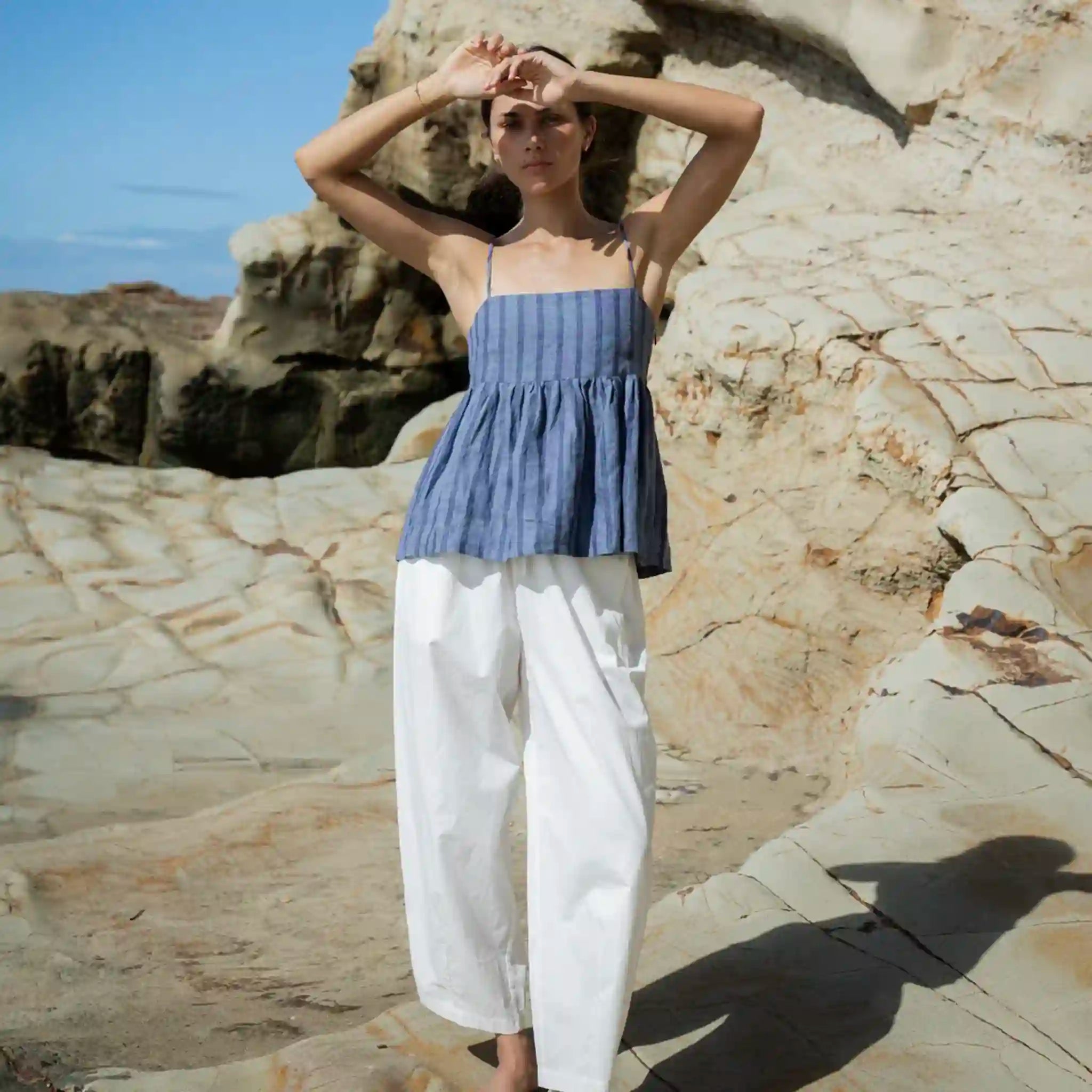 Woman in a blue top and white pants standing against a rocky background