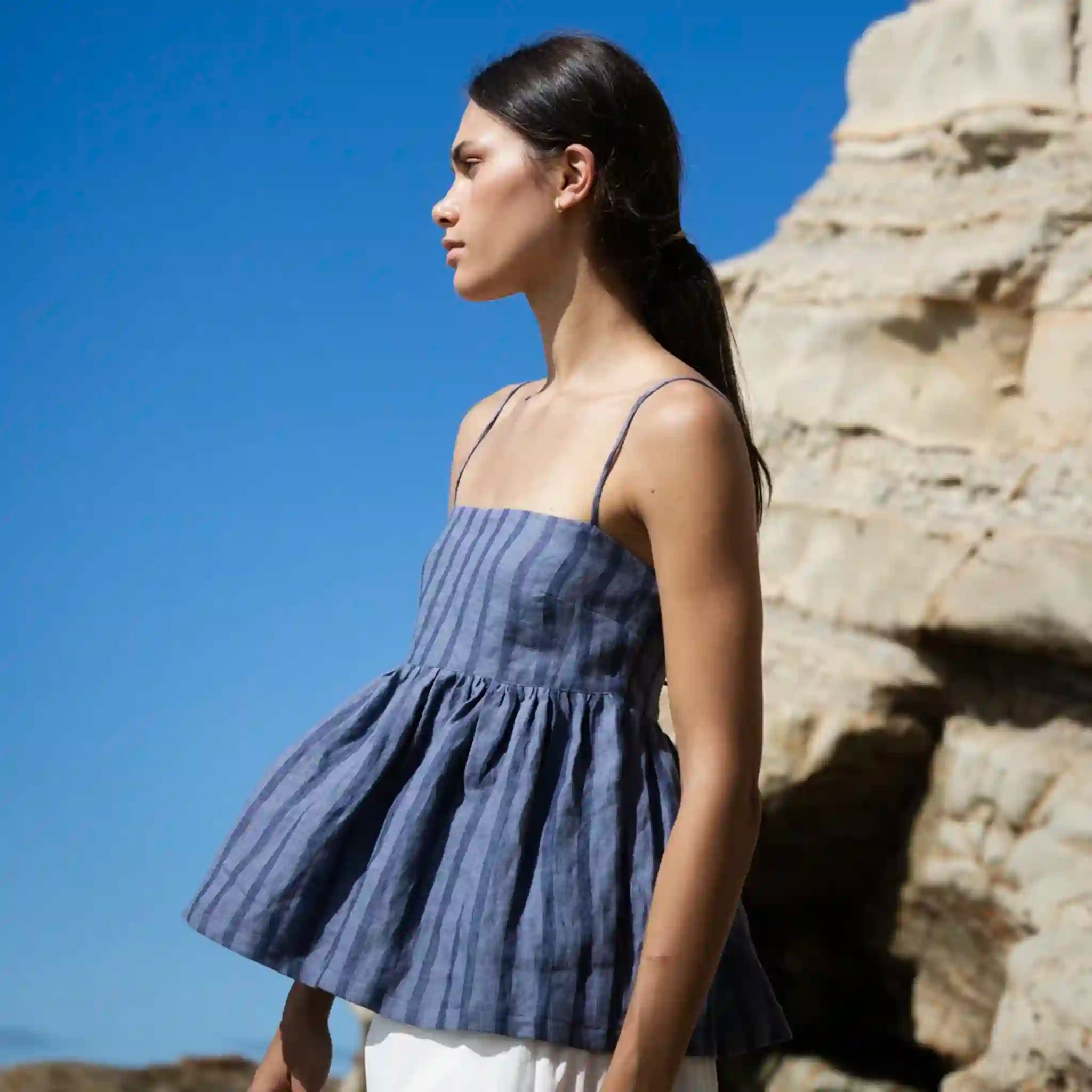 Woman wearing a blue striped dress standing against a rocky background