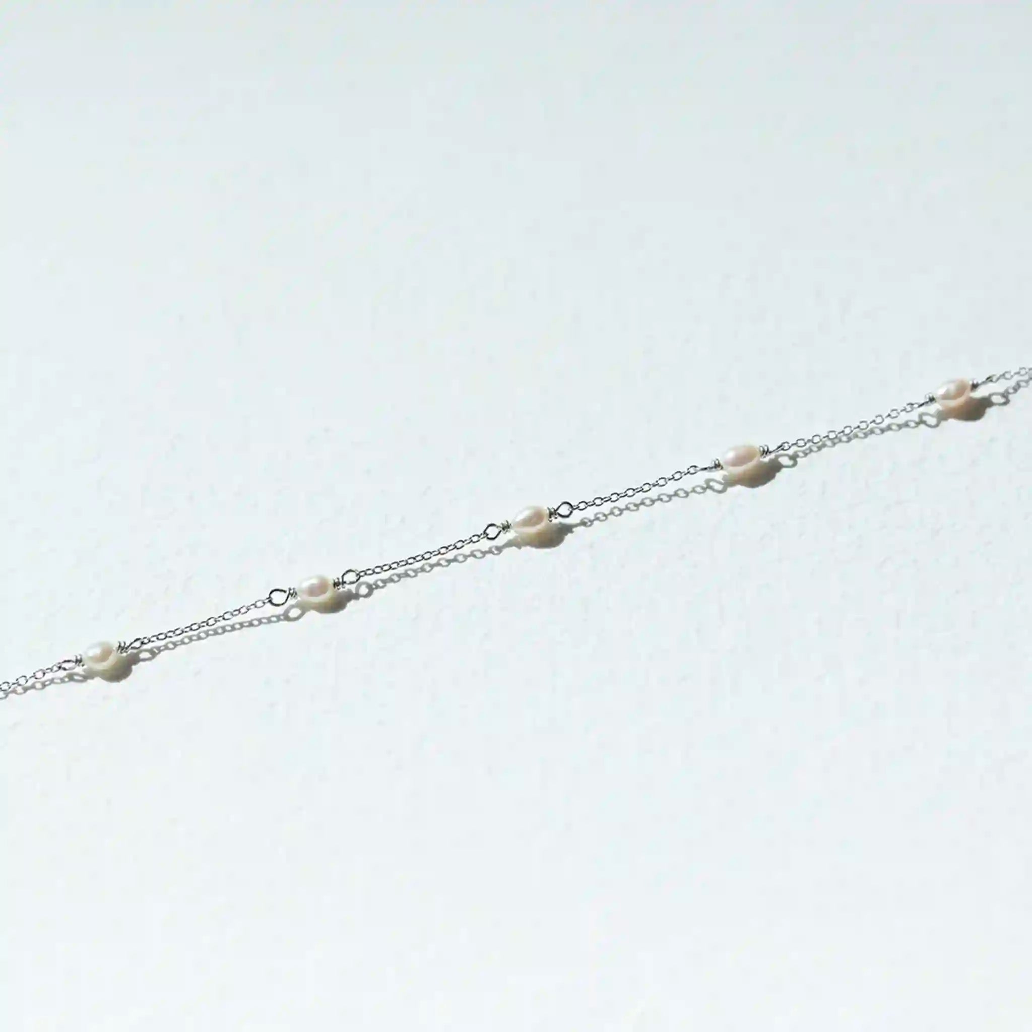 Silver chain with small white beads on a light gray background
