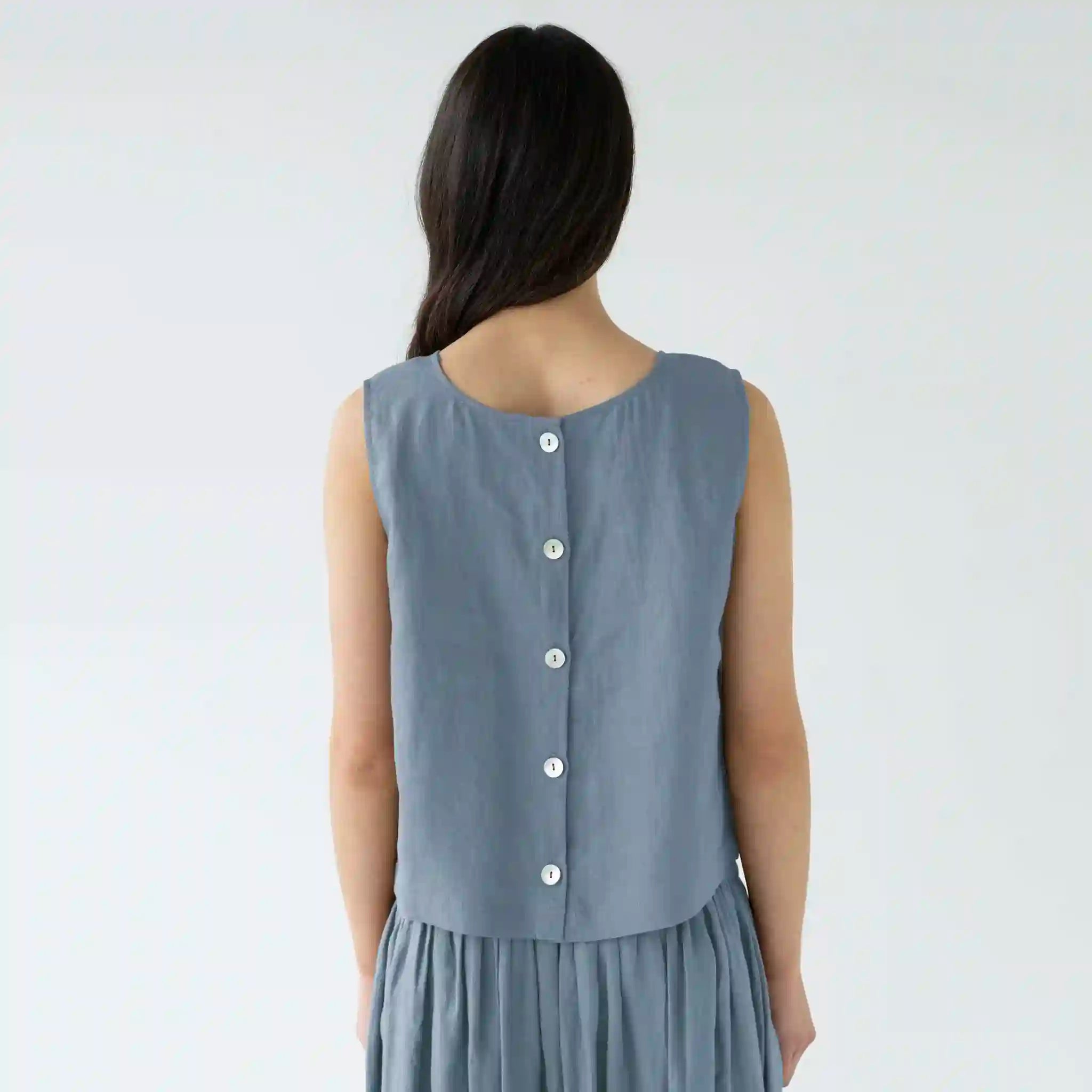 Woman wearing a sleeveless gray dress with buttons on a plain background