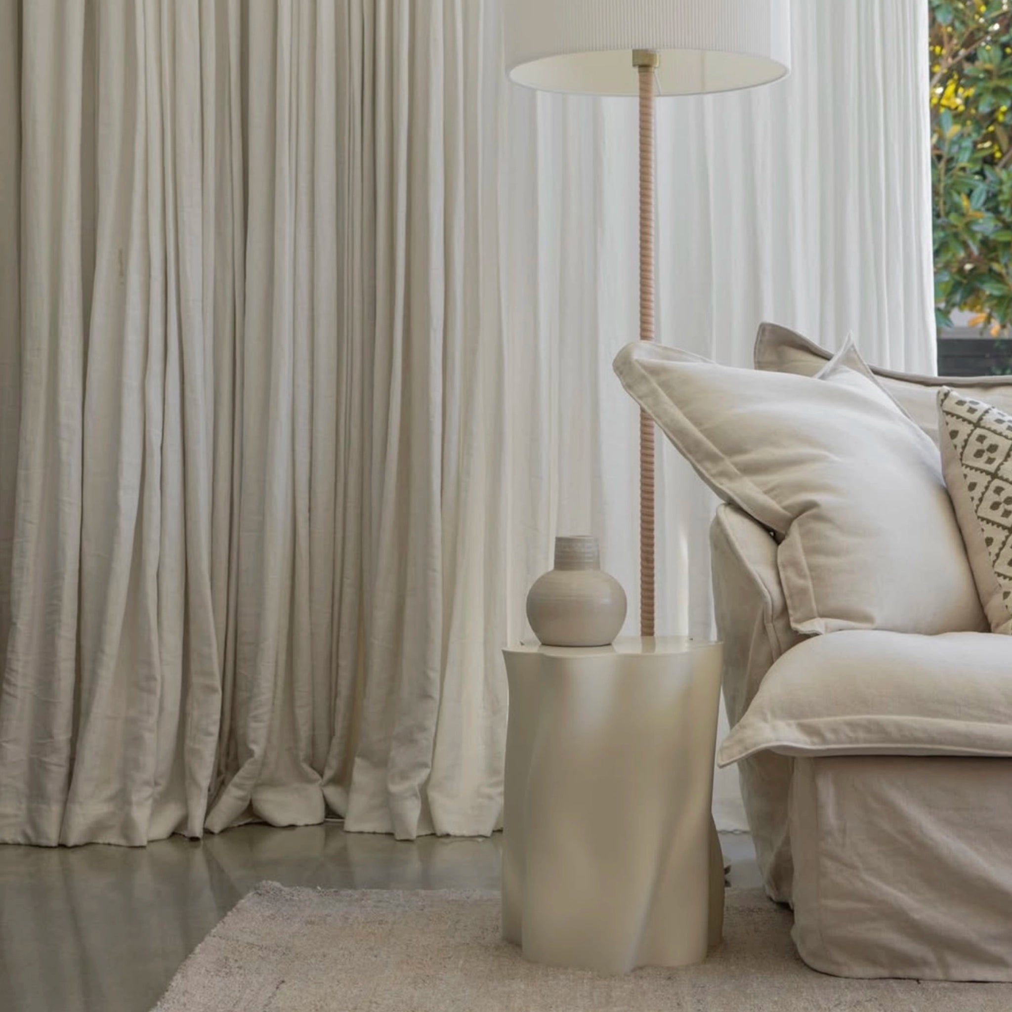 Beige living room with a sofa, side table, and lamp against a curtain backdrop