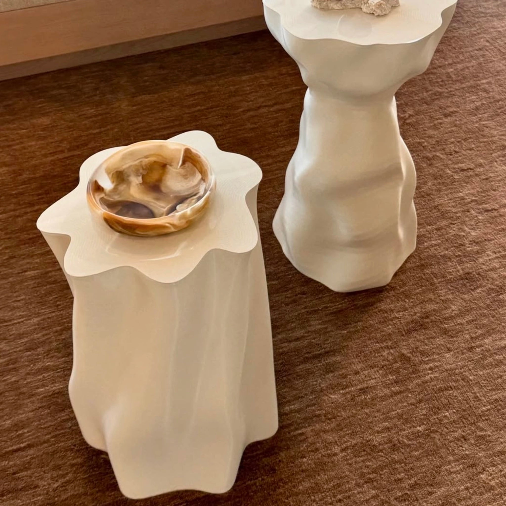 Two white decorative tables with a bowl on a brown surface