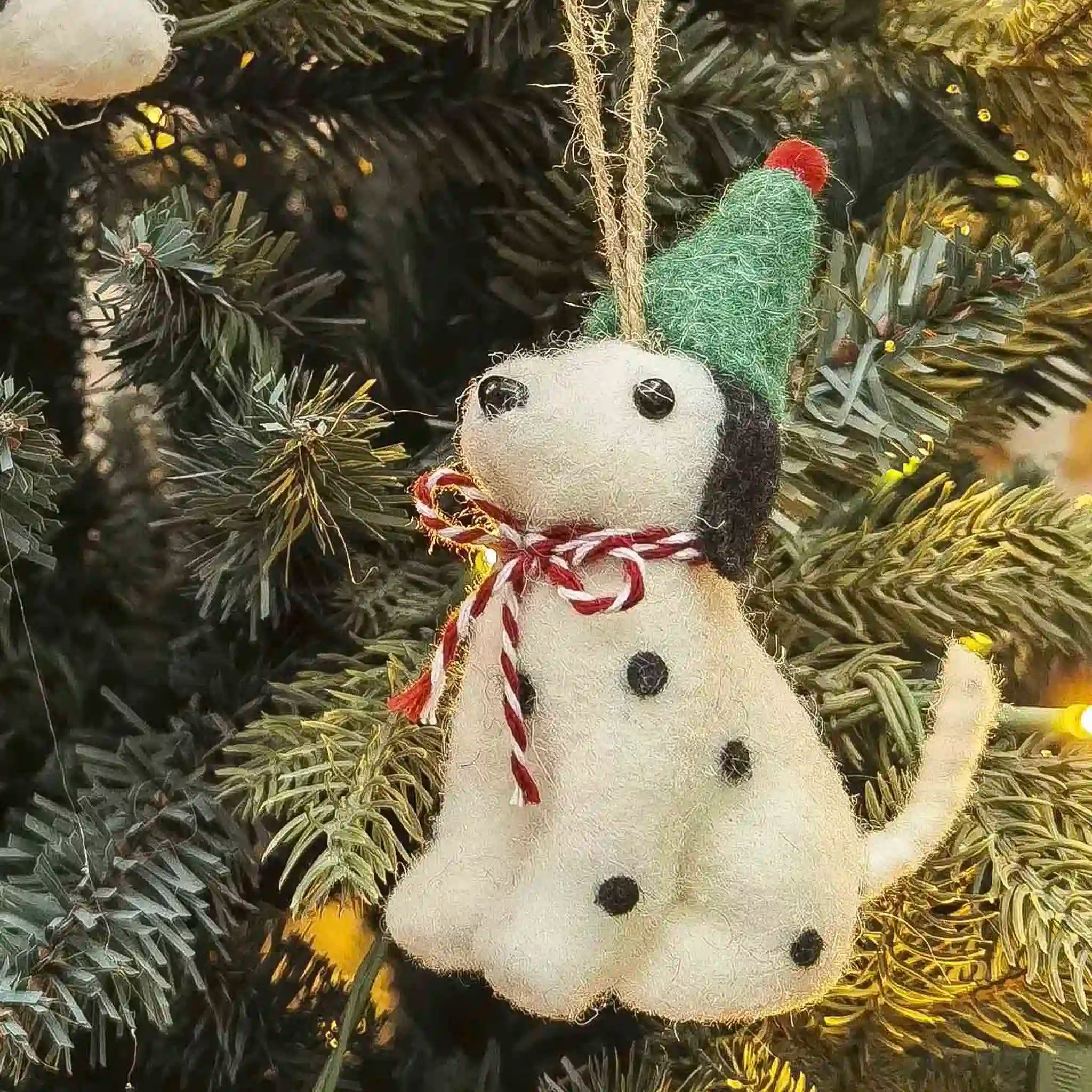 Felt dog ornament with a green hat and red bow tie hanging on a Christmas tree.