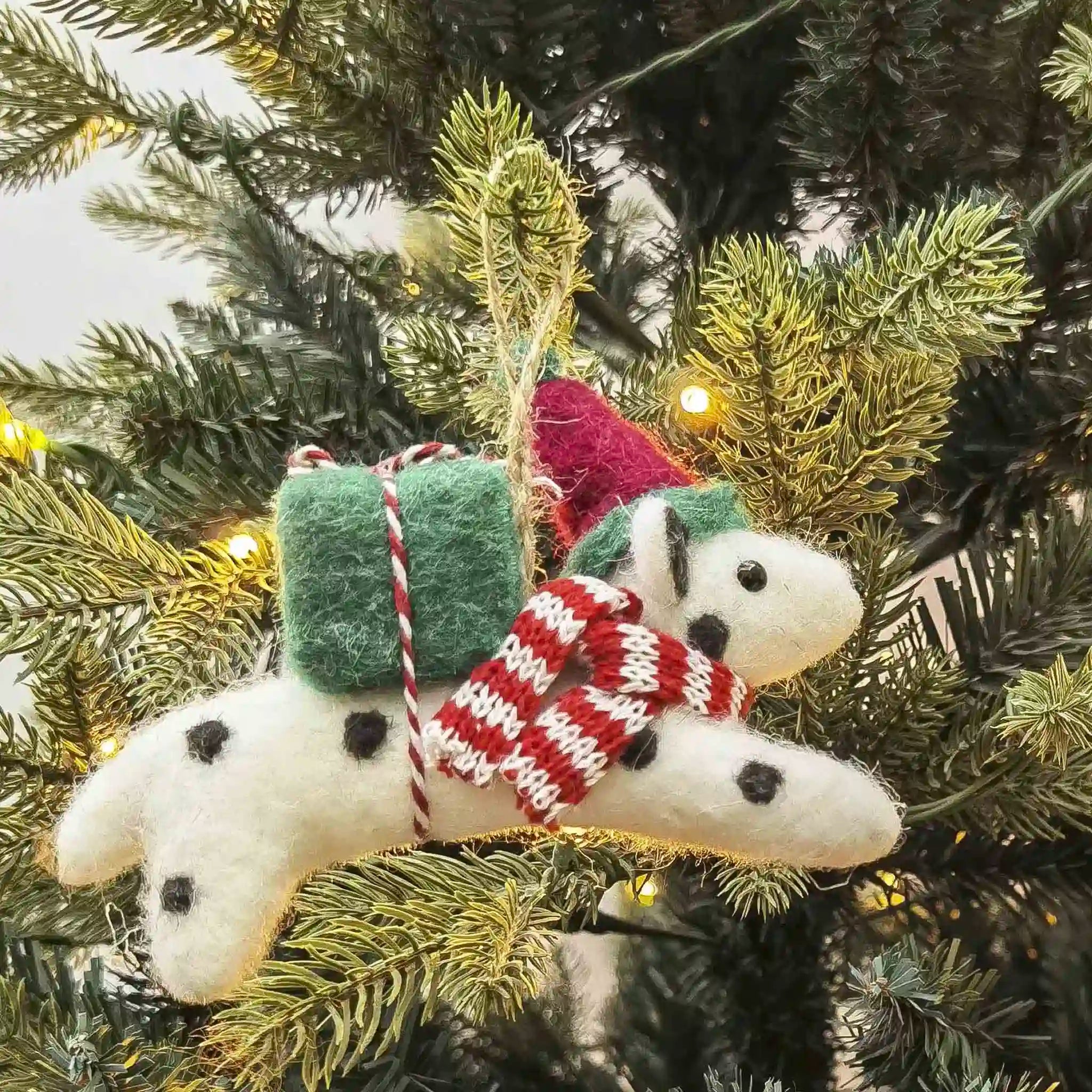 Decorative dog ornament with a green bag and red scarf hanging on a Christmas tree.
