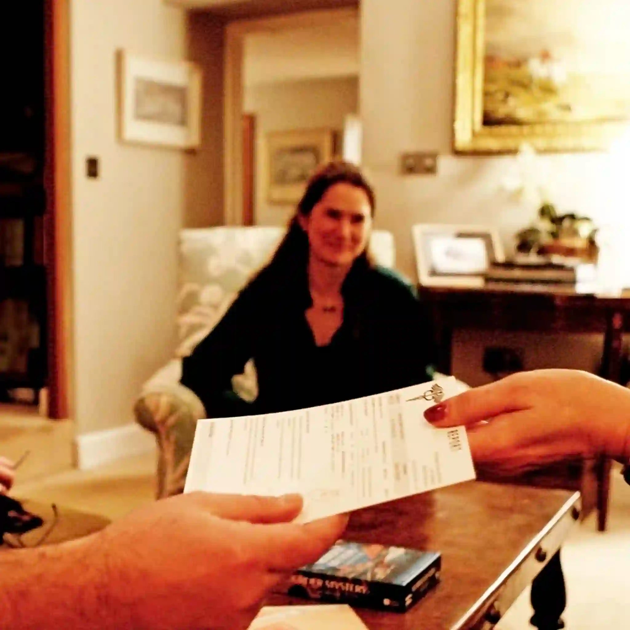 Person handing over a piece of paper to another person in a living room setting.