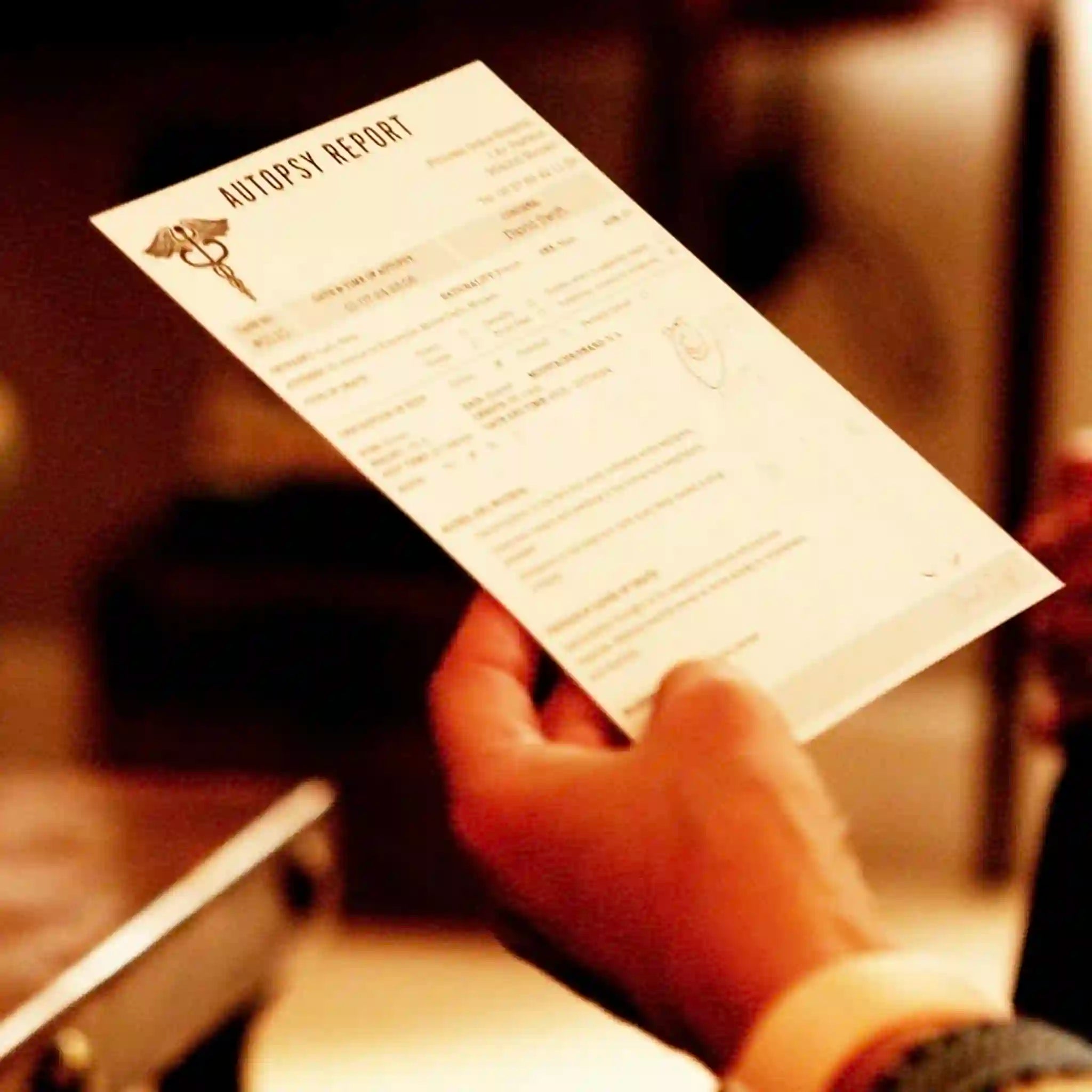 Hand holding an 'Autopsy Report' document with a blurred background
