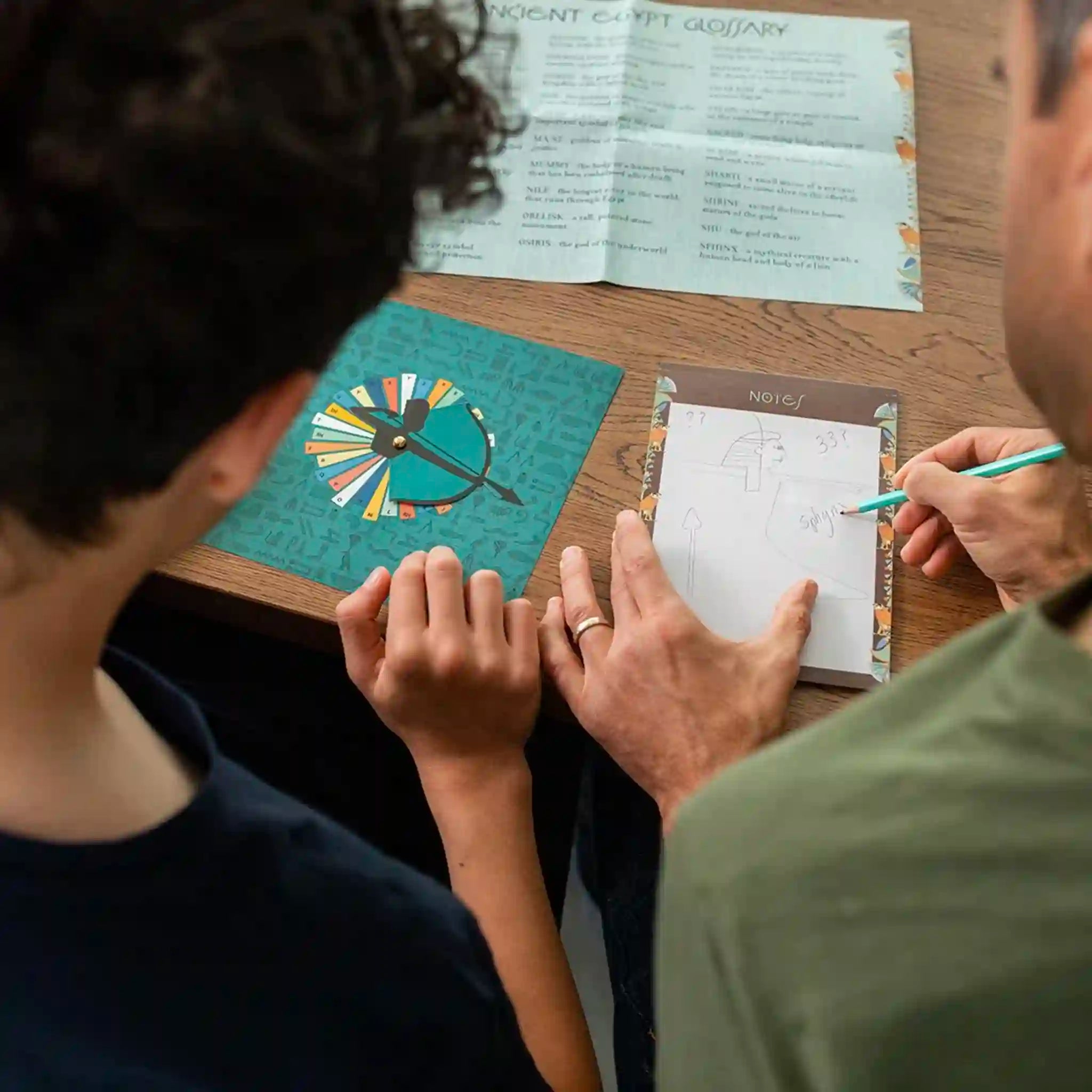 Two people sitting at a table with a board game and paper in front of them