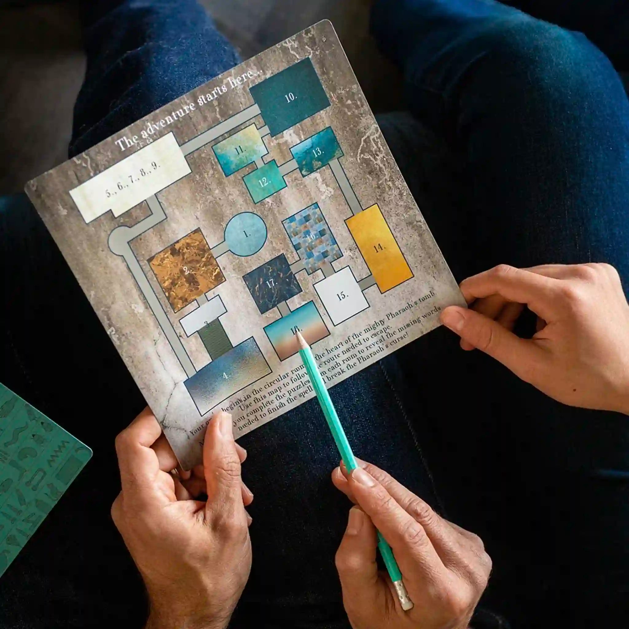 Person holding a detailed map and a pen, sitting on a dark surface.