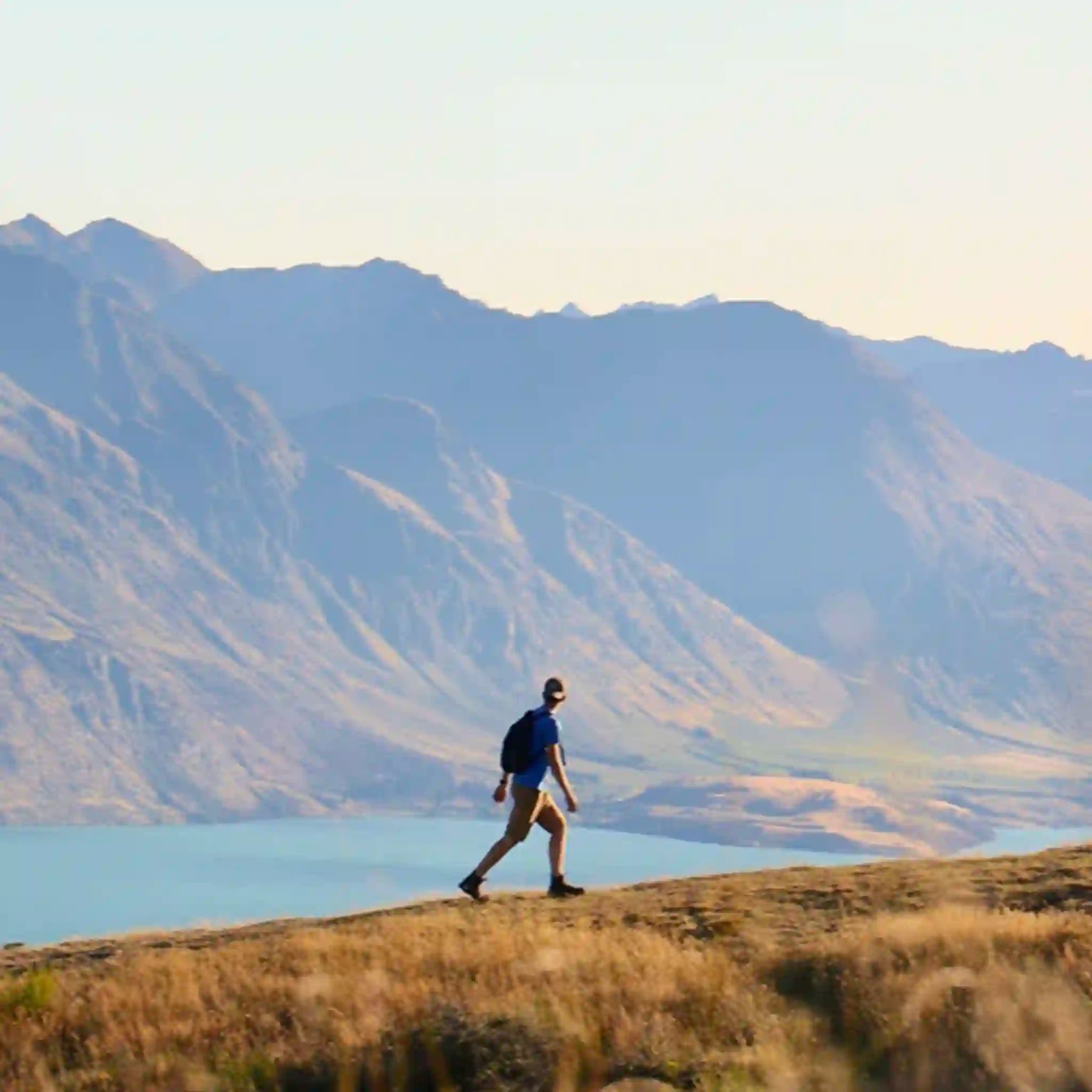 Person walking on a hill with mountains and lake in the background
