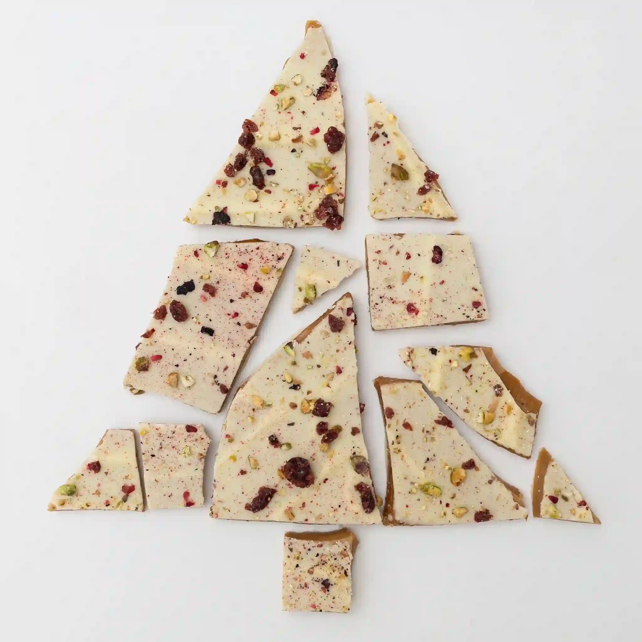 Broken pieces of white chocolate bark with nuts and cranberries on a light gray background